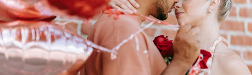 Two people embracing with a brick wall and red artificial roses flowers in the background
