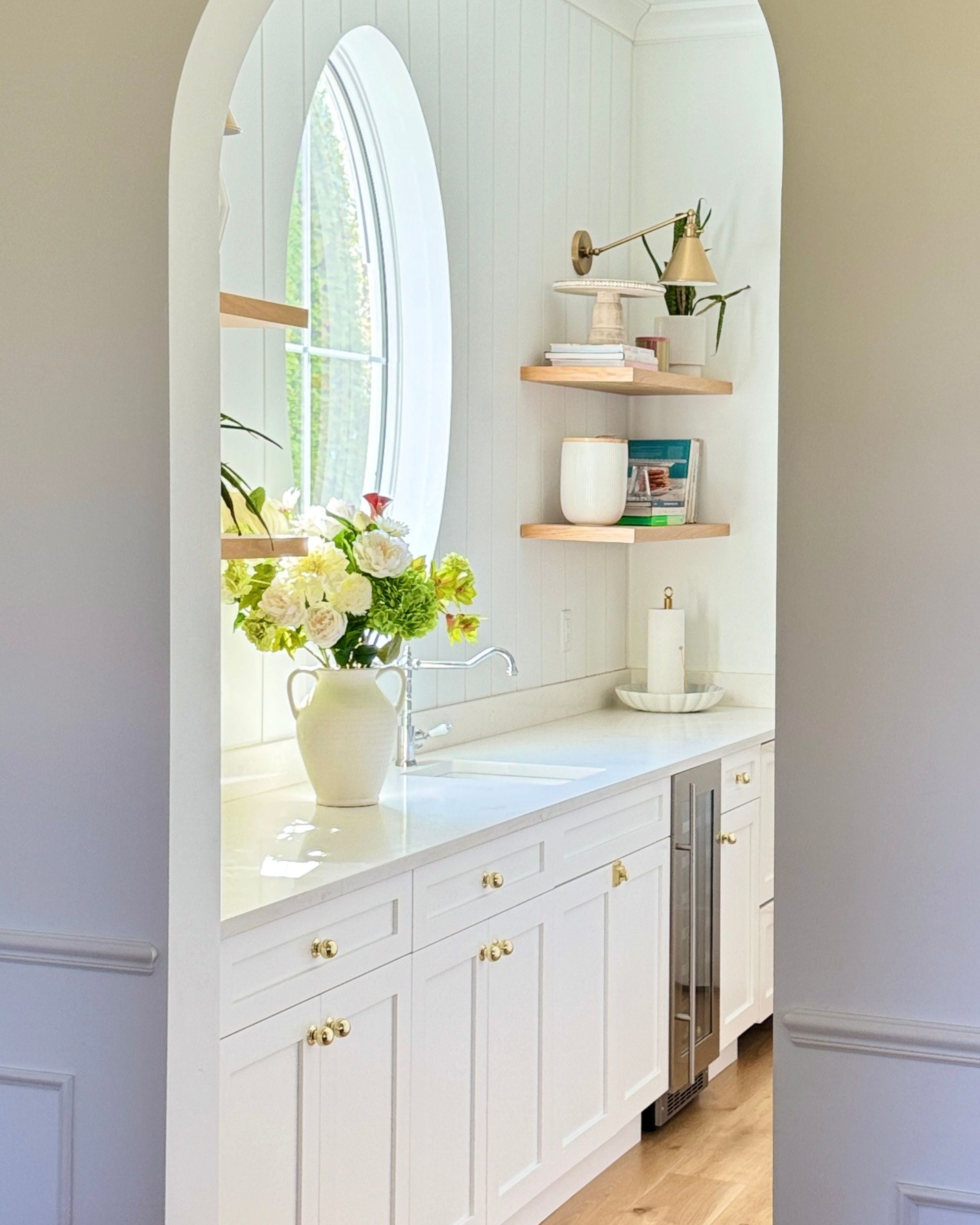 White kitchen with arched window, countertop decor, a vase of white and green realistic artificial flowers and open shelves. Faux peonies, faux roses, faux hydrangea, and faux orchids in an artificial flower bouquet for My Faux Florist Canada.
