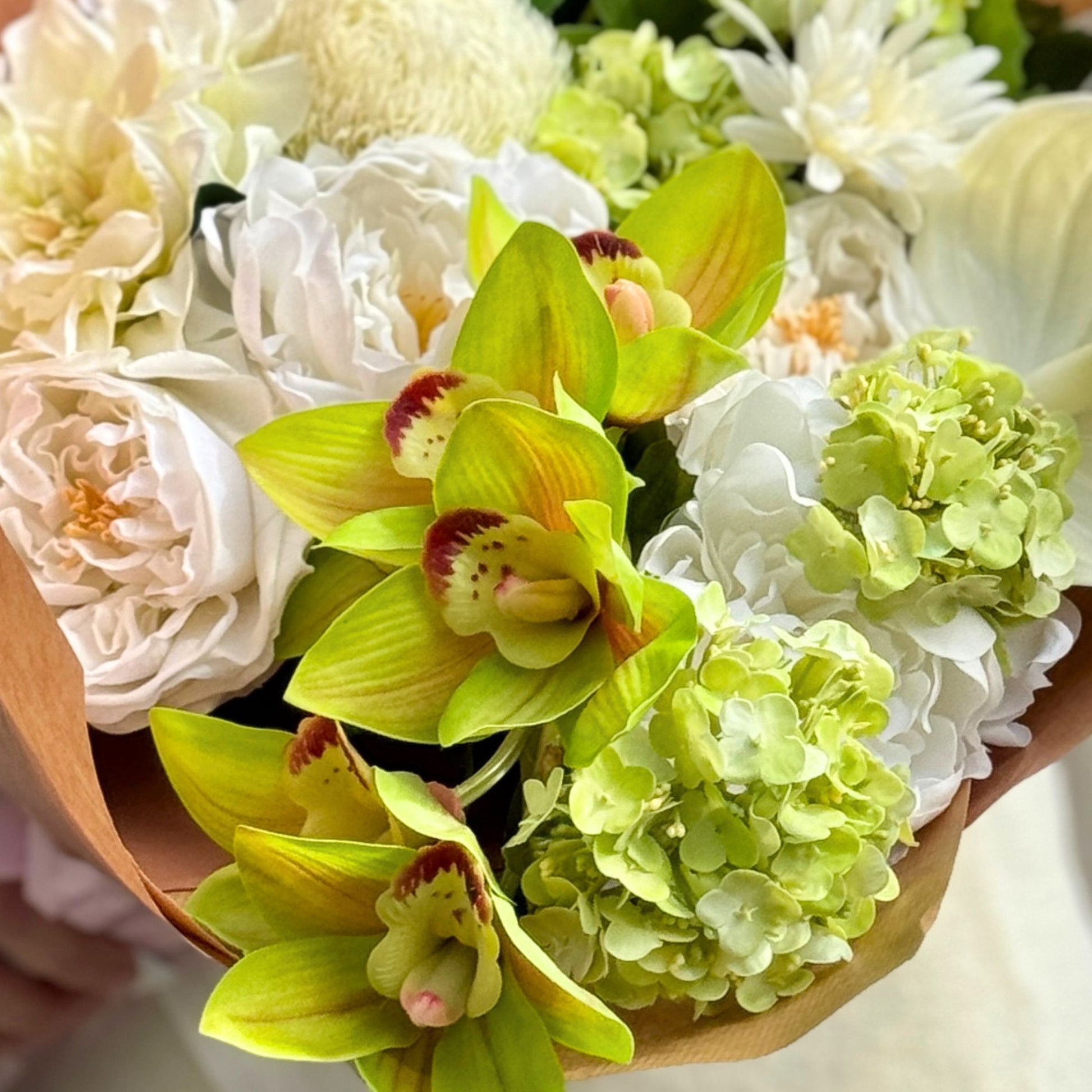Bouquet of realistic artificial flowers in white and green held by a person. Faux peonies, faux roses, faux hydrangea, and faux orchids in an artificial flower bouquet for My Faux Florist Canada.