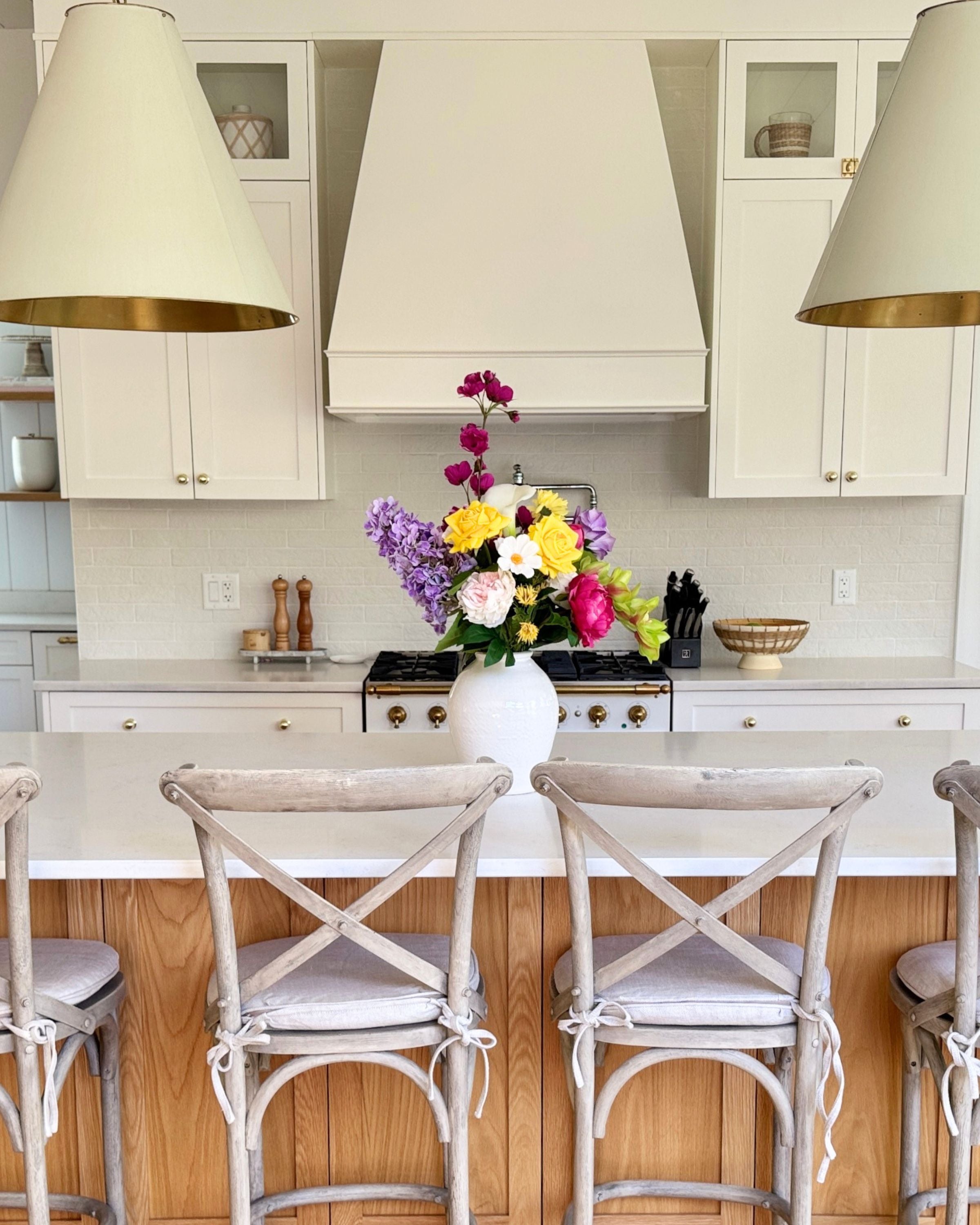 Kitchen with white cabinets, a stove, and a vase of colorful realistic artificial flowers on the counter. Faux peonies, faux roses, faux hydrangea, and faux orchids in an artificial flower bouquet for My Faux Florist Canada.