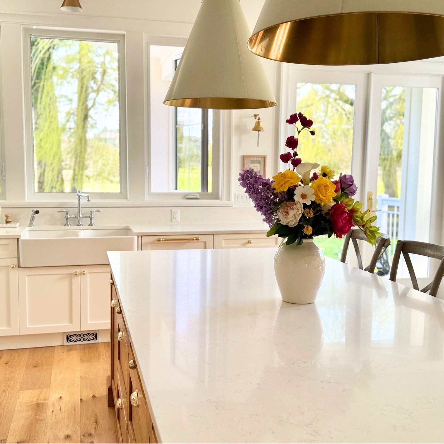 Modern kitchen with white countertops, gold pendant lights, and a vase of realistic artificial flowers. Faux peonies, faux roses, faux hydrangea, and faux orchids in an artificial flower bouquet for My Faux Florist Canada.