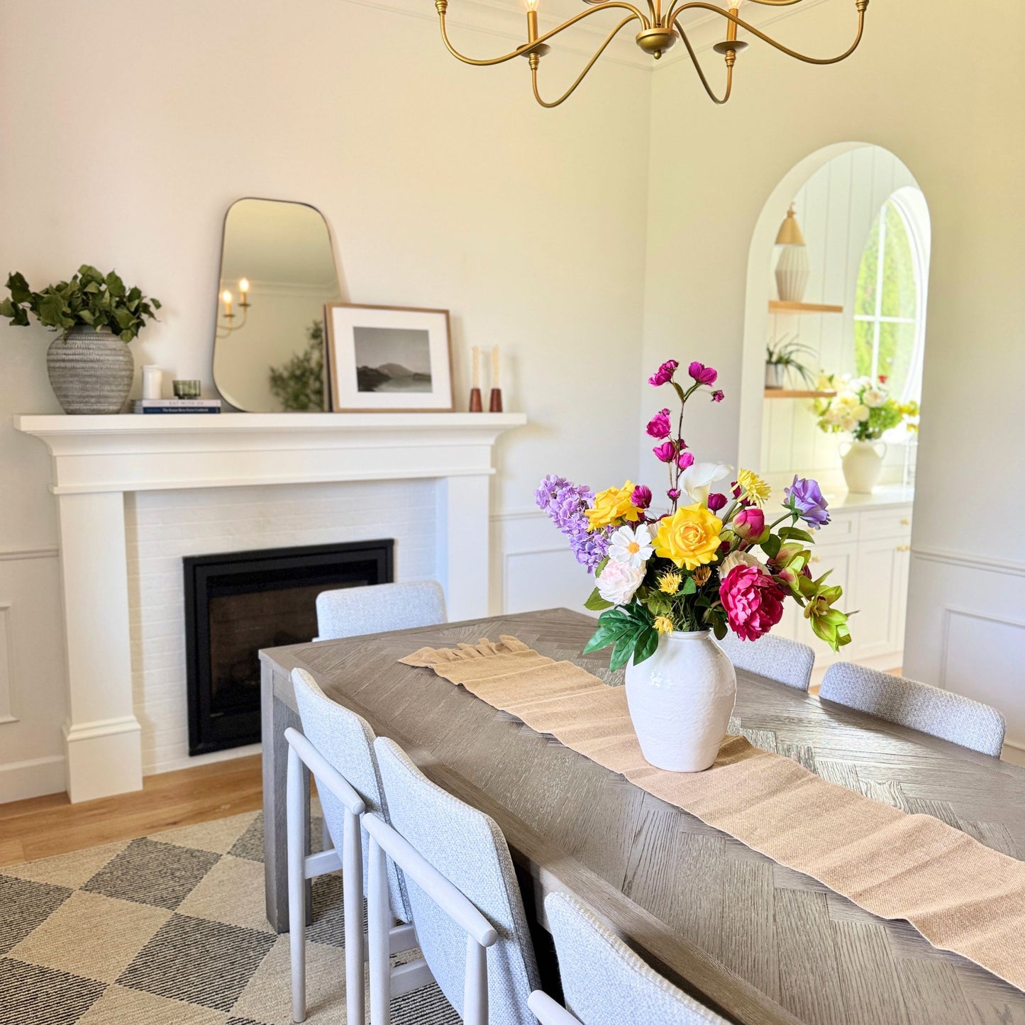 Dining room with a fireplace, mirror, and a realistic artificial floral arrangement on a table. Faux peonies, faux roses, faux hydrangea, and faux orchids in an artificial flower bouquet for My Faux Florist Canada.