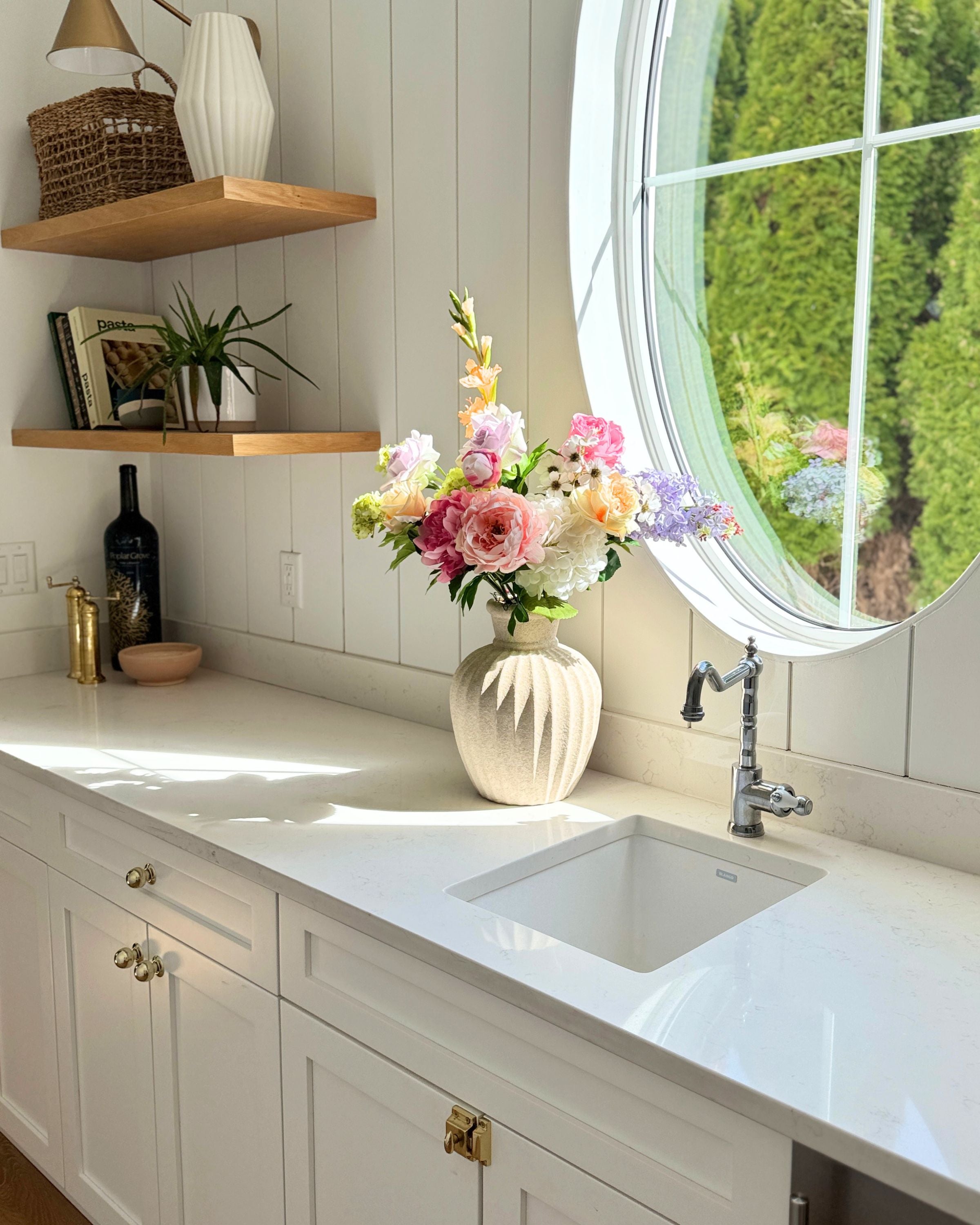 A large vase of colourful realistic artificial flowers sit on a kitchen counter next to a small sink and window. Faux peonies, faux roses, faux hydrangea, and faux orchids in an artificial flower bouquet for My Faux Florist Canada.