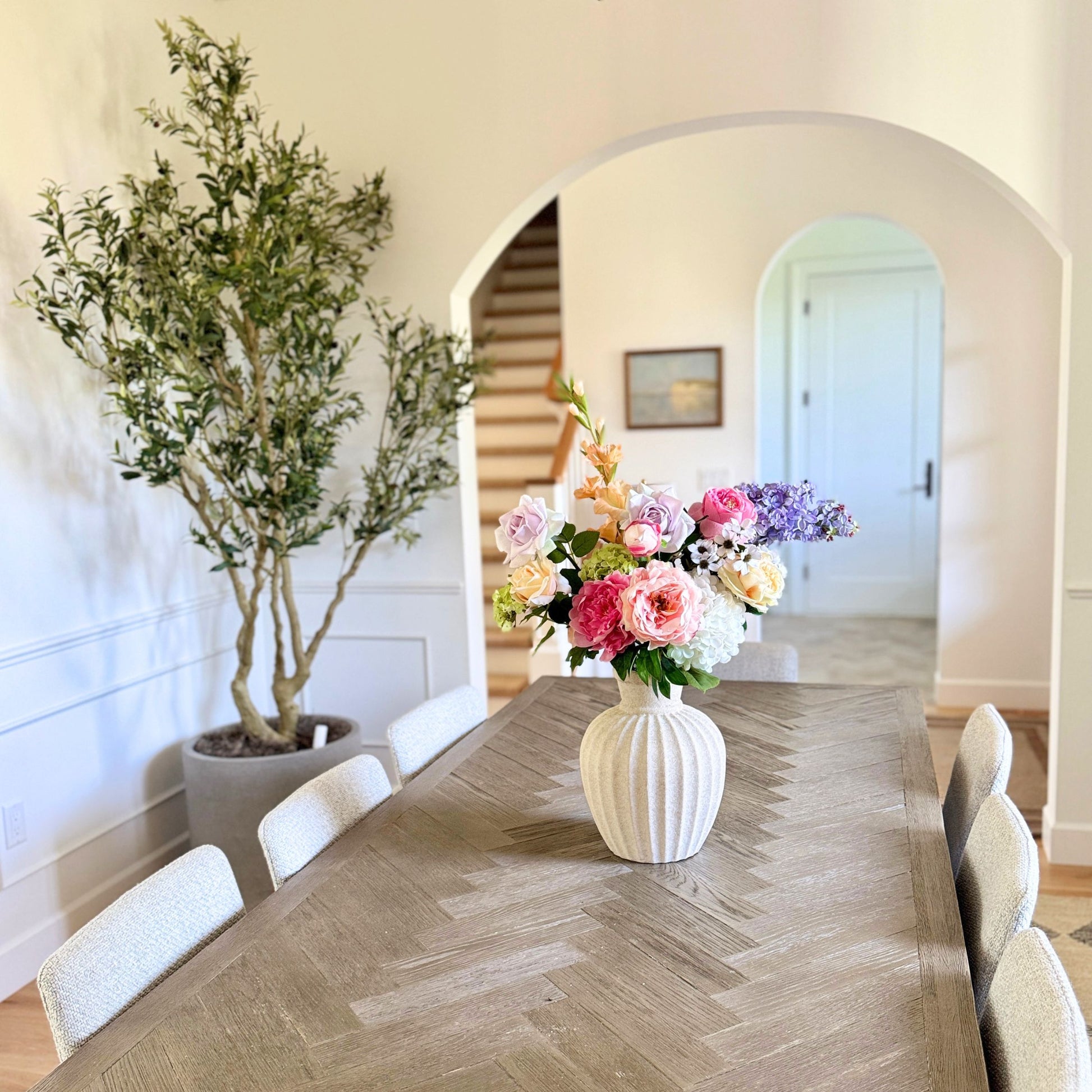 Dining room with a long table, chairs, and a vase of realistic artificial flowers. Faux peonies, faux roses, faux hydrangea in an artificial flower bouquet for My Faux Florist Canada.