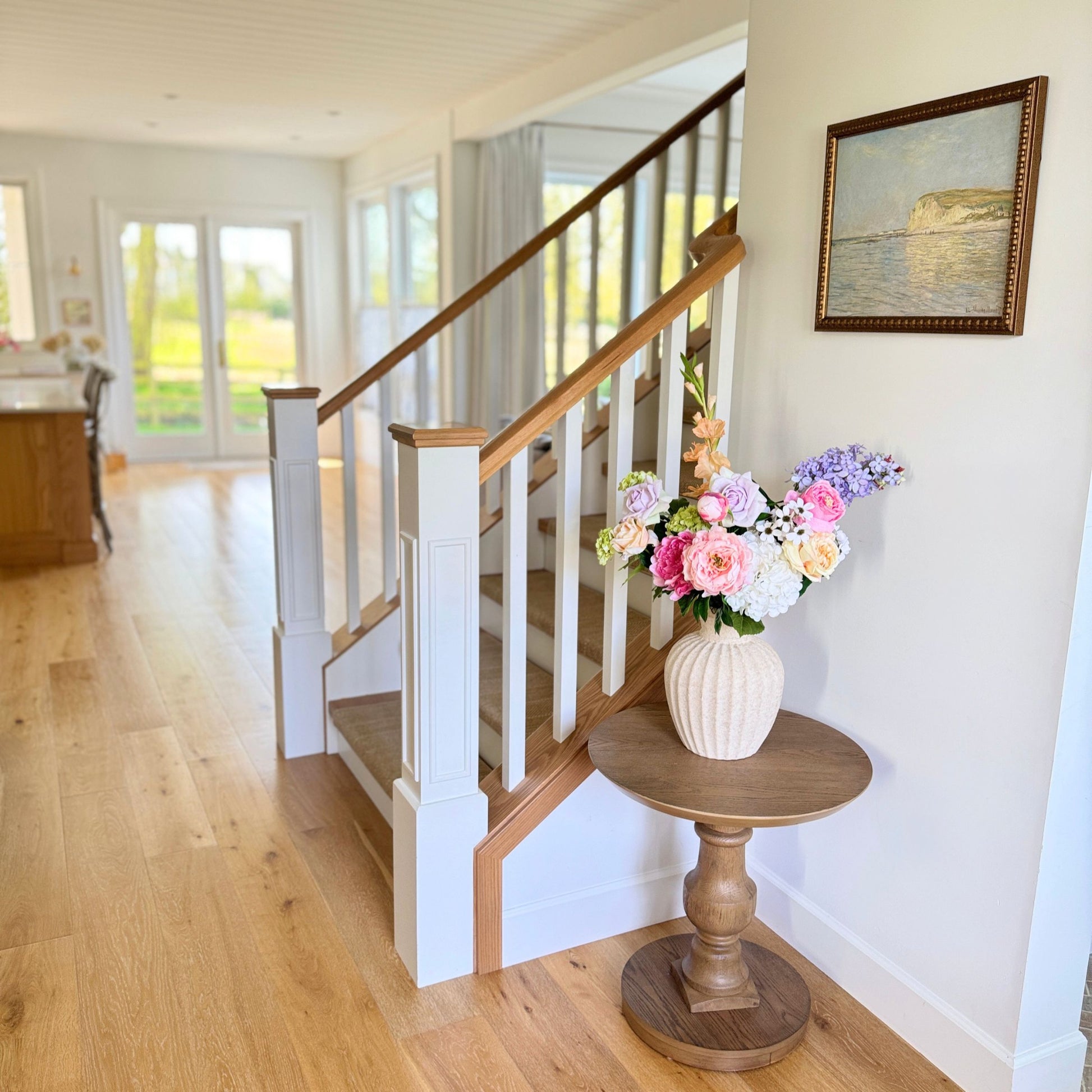 Staircase with wooden handrail and a vase of realistic artificial flowers on a small table in a well-lit room. Faux peonies, faux roses, faux hydrangea in an artificial flower bouquet for My Faux Florist Canada.
