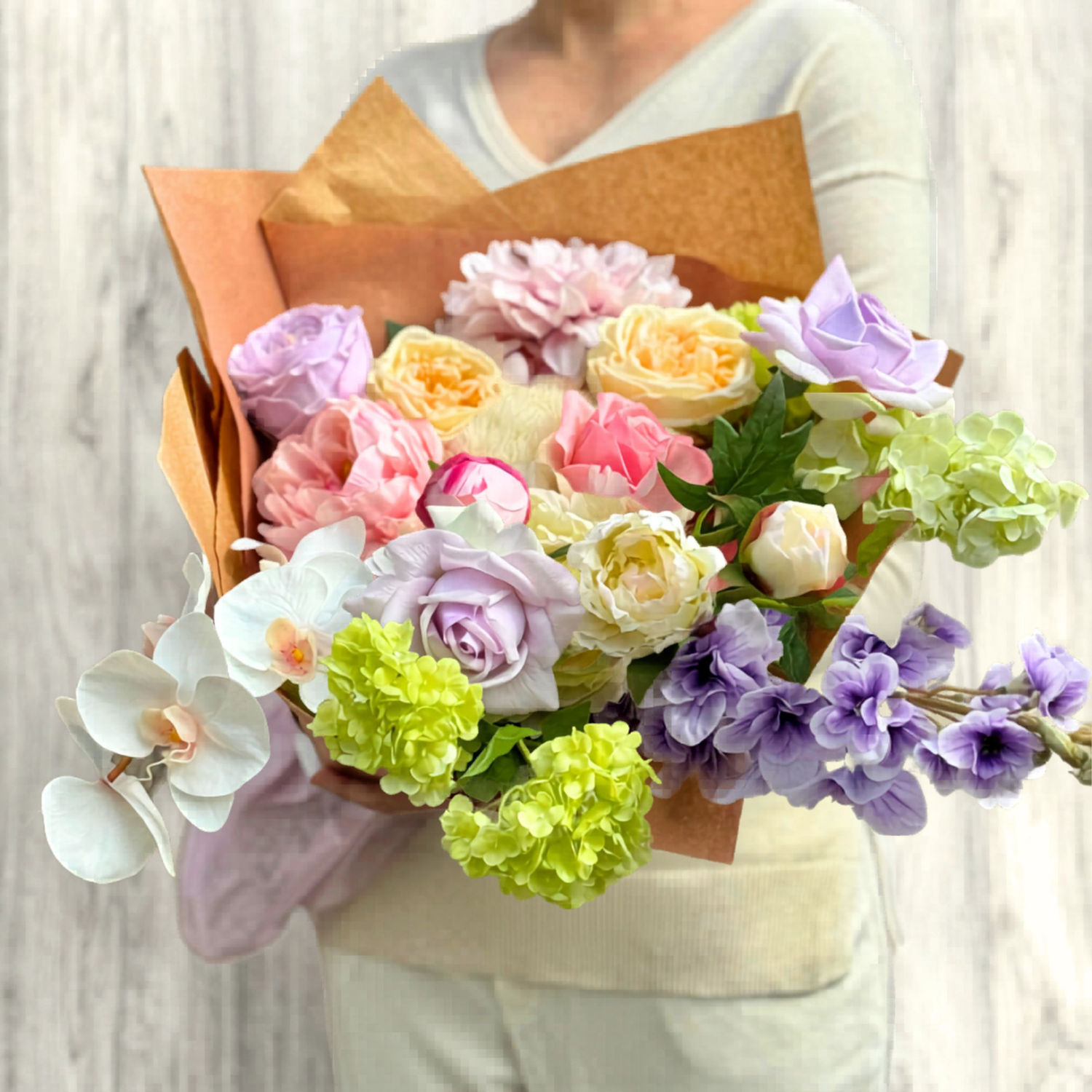 Bouquet of colorful realistic artificial flowers held by a person against a neutral background. Faux peonies, faux roses, faux hydrangea, and faux orchids in an artificial flower bouquet for My Faux Florist Canada.