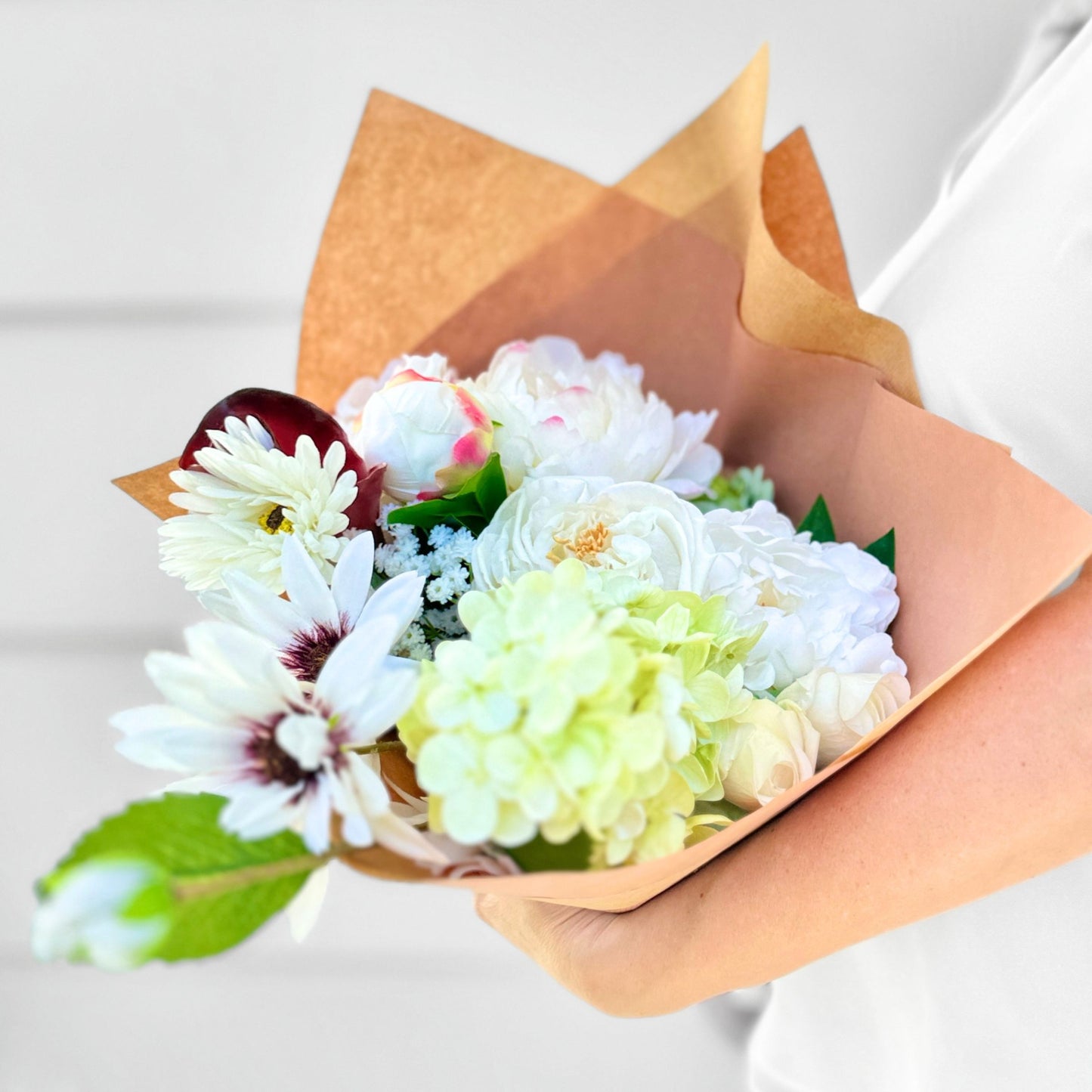 Bouquet of realistic artificial flowers wrapped in brown paper held by a person.  For My Faux Florist Canada.
