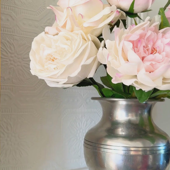 Video of silver vase containing realistic artificial flowers sits on a fireplace mantel.  The vase includes artificial roses, artificial peonies and artificial hydrangea in shades of pink, white and cream.  For My Faux Florist Canada.
