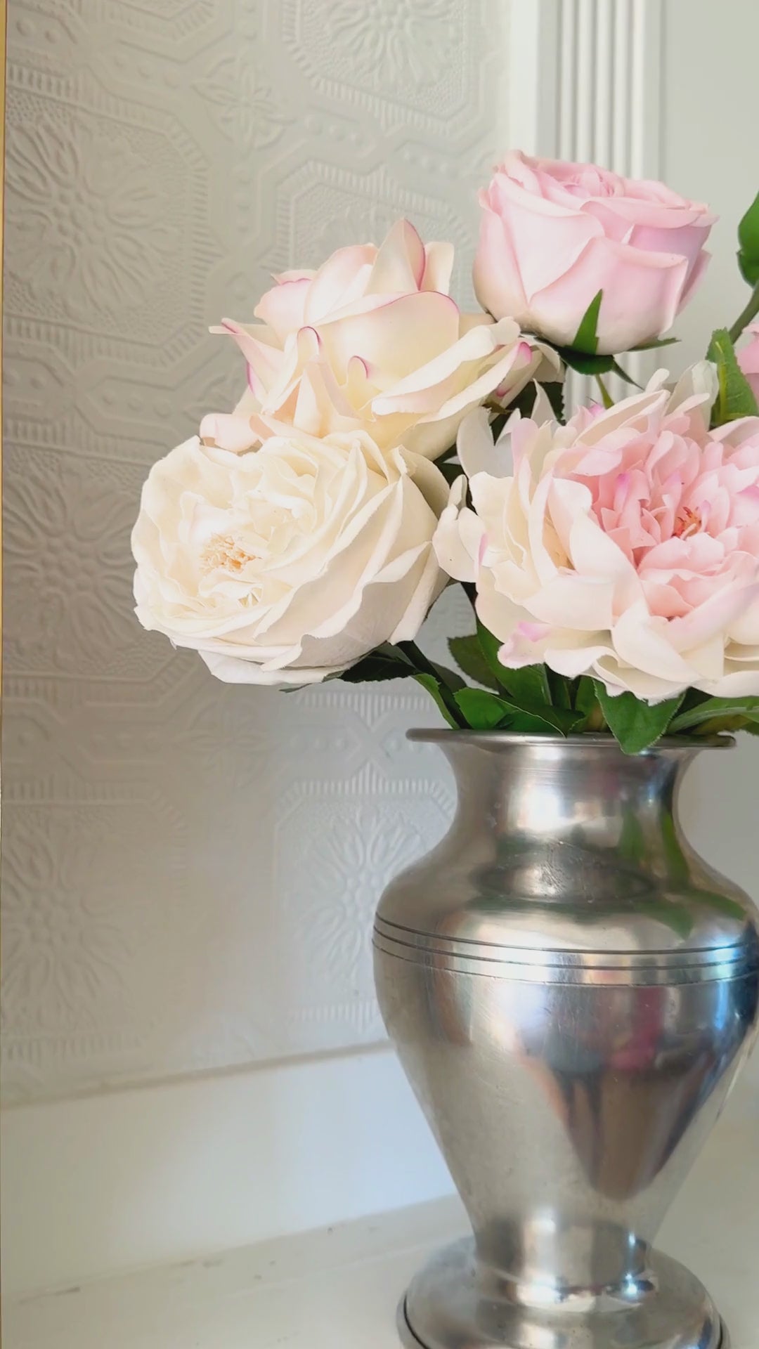 Video of silver vase containing realistic artificial flowers sits on a fireplace mantel.  The vase includes artificial roses, artificial peonies and artificial hydrangea in shades of pink, white and cream.  For My Faux Florist Canada.