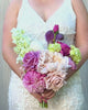 Bride holding a realistic artificial flower bridal bouquet featuring antique cream artificial roses, dusty mauve artificial roses, blush artificial peonies, pink artificial dahlias, pale green artificial hydrangeas, green artificial peonies, and deep wine artificial calla lilies — from My Faux Florist Canada.