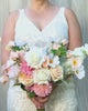 Bride holding a realistic artificial flower bridal bouquet featuring white artificial roses, blush artificial peonies, apricot artificial tulips, cream artificial tea roses, pink artificial hydrangeas, and white artificial cosmos — from My Faux Florist Canada.