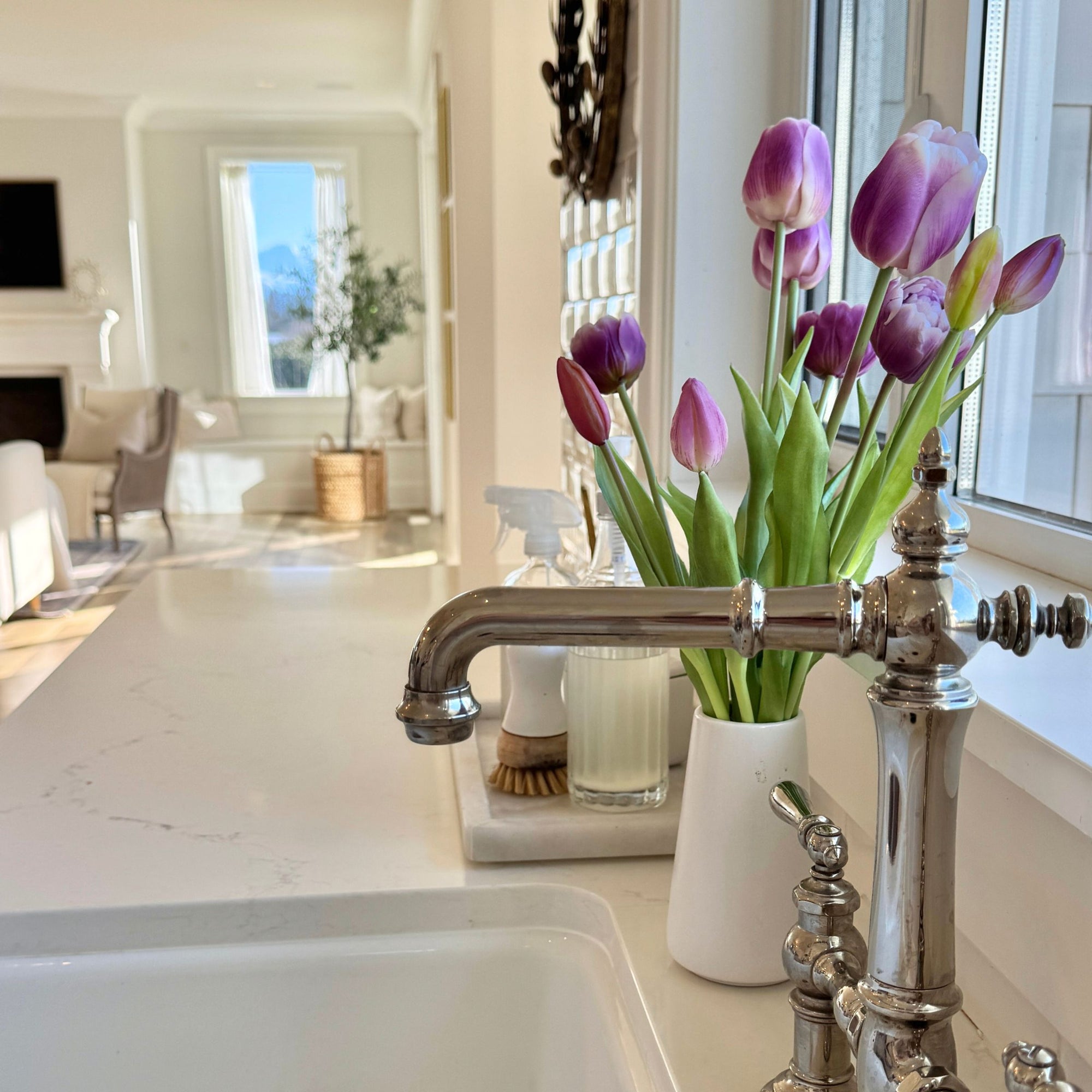 Purple artificial tulips in a white vase on a kitchen counter with a silver faucet,  for My Faux Florist Canada.