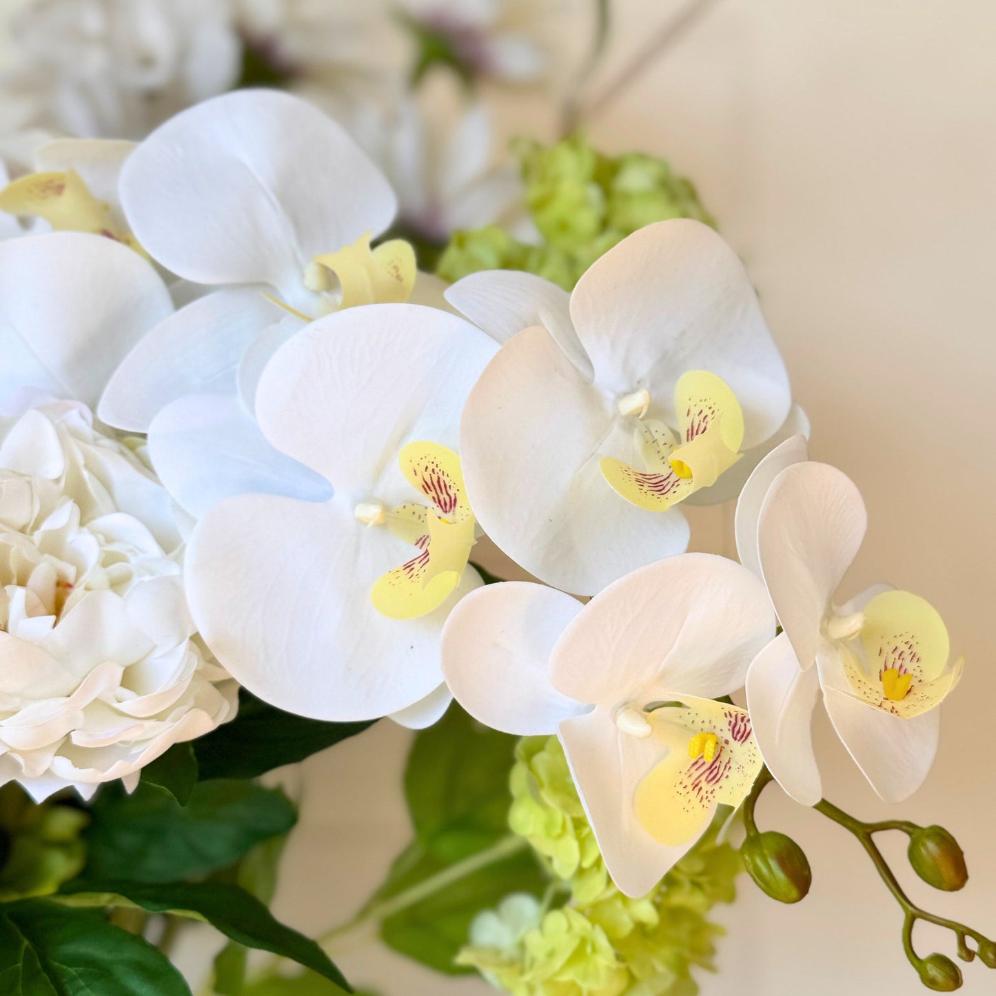 Close-up of white realistic artificial orchids with yellow centers in a bouquet. Faux peonies, faux roses, faux hydrangea, and faux orchids in an artificial flower bouquet for My Faux Florist Canada.