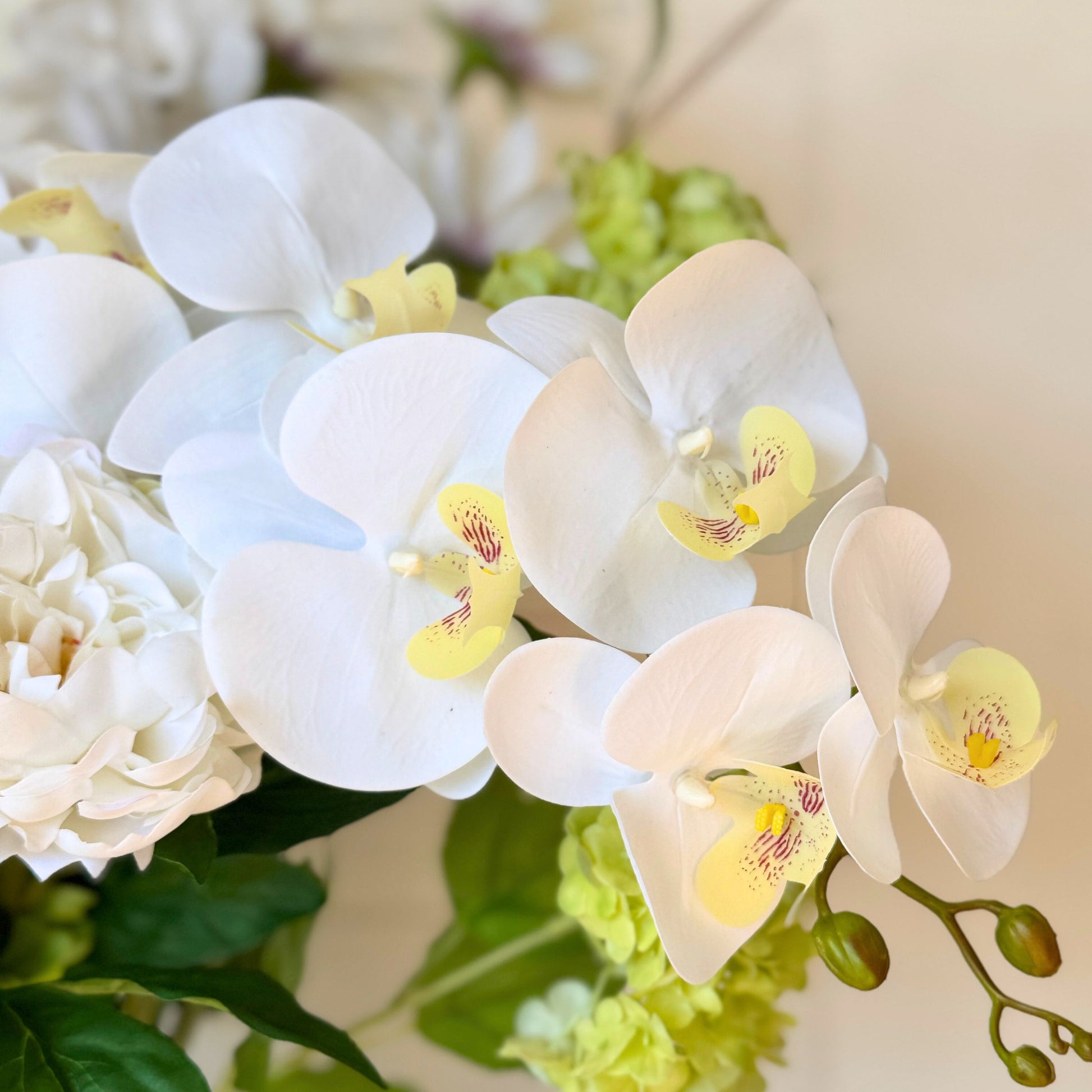 Close-up of white realistic artificial orchids with yellow centers in a bouquet. Faux peonies, faux roses, faux hydrangea, and faux orchids in an artificial flower bouquet for My Faux Florist Canada.