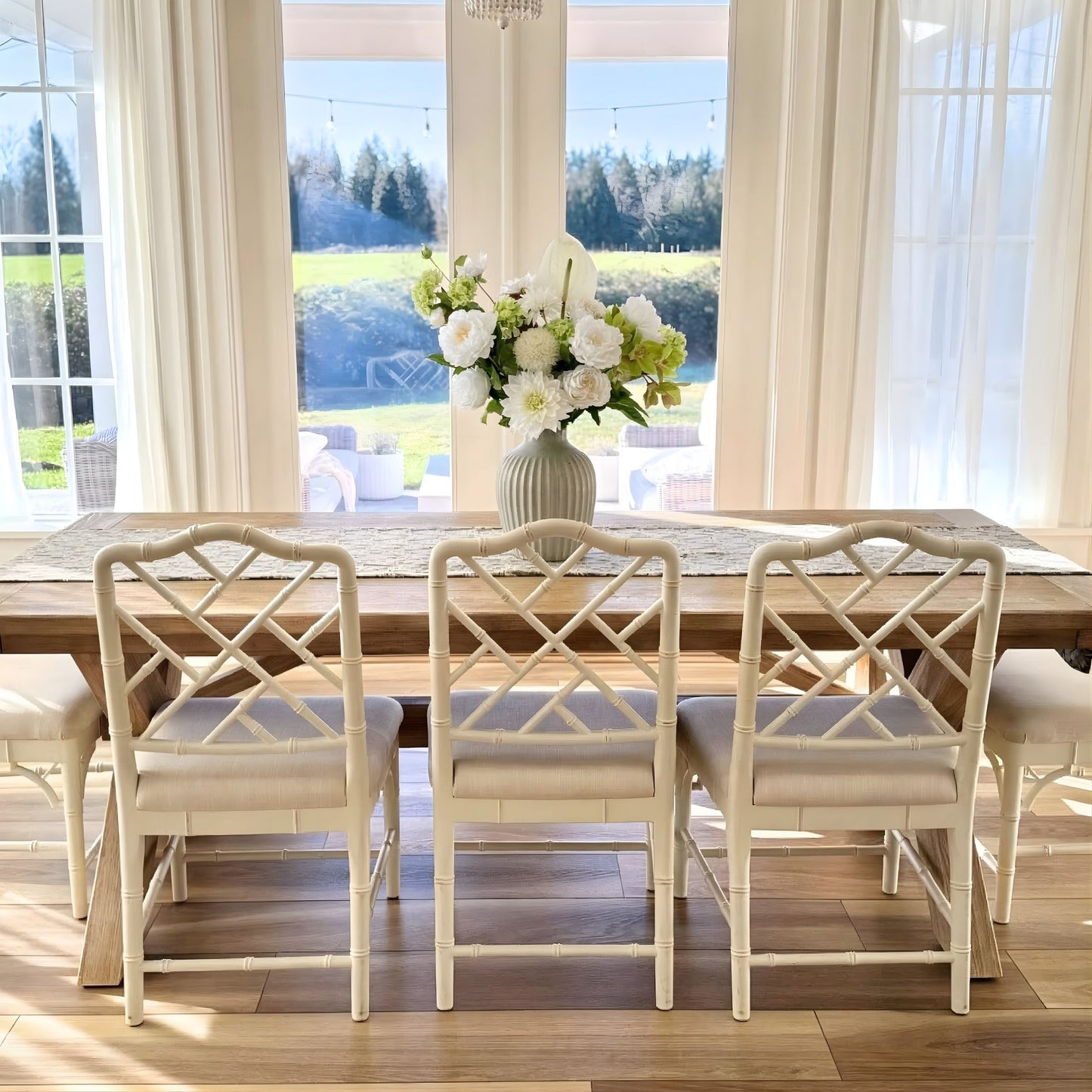 Dining room with wooden table and white chairs, large windows with curtains, and a vase of realistic artificial flowers. Faux peonies, faux roses, faux hydrangea, and faux orchids in an artificial flower bouquet for My Faux Florist Canada.