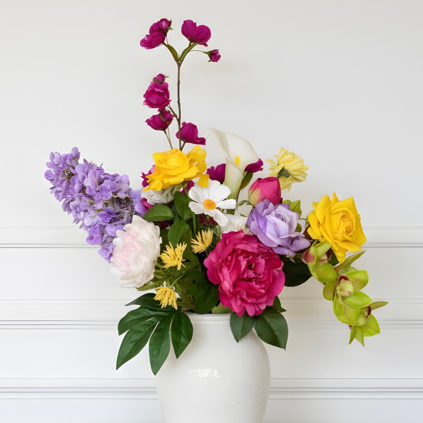 Colorful flower arrangement of realistic artificial flowers in a white vase on a light wooden background. Faux peonies, faux roses, faux hydrangea, and faux orchids in an artificial flower bouquet for My Faux Florist Canada.