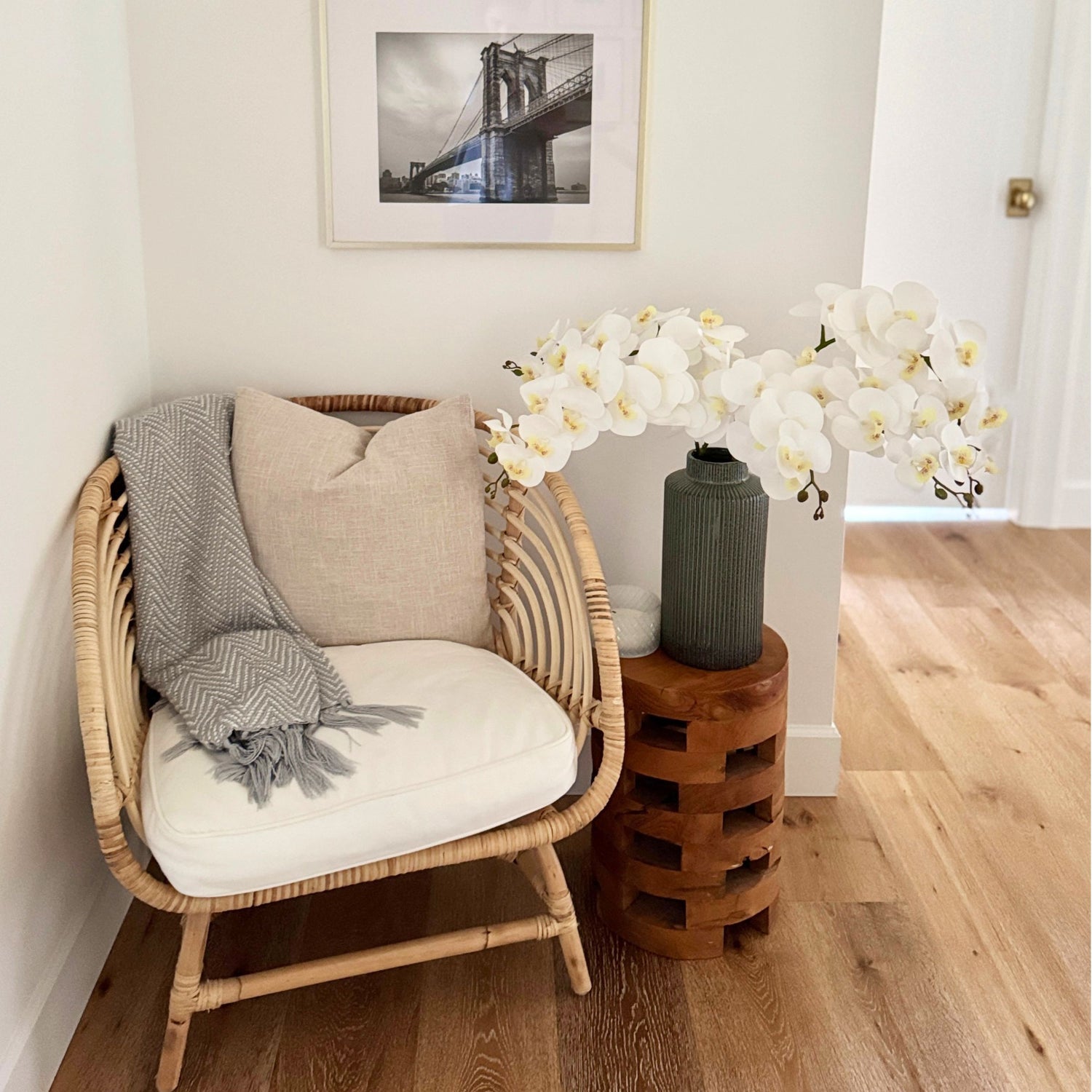 Wicker chair with white cushion, gray blanket, and wooden side table with vase or white realistic artificial orchids - for My Faux Florist Canada.