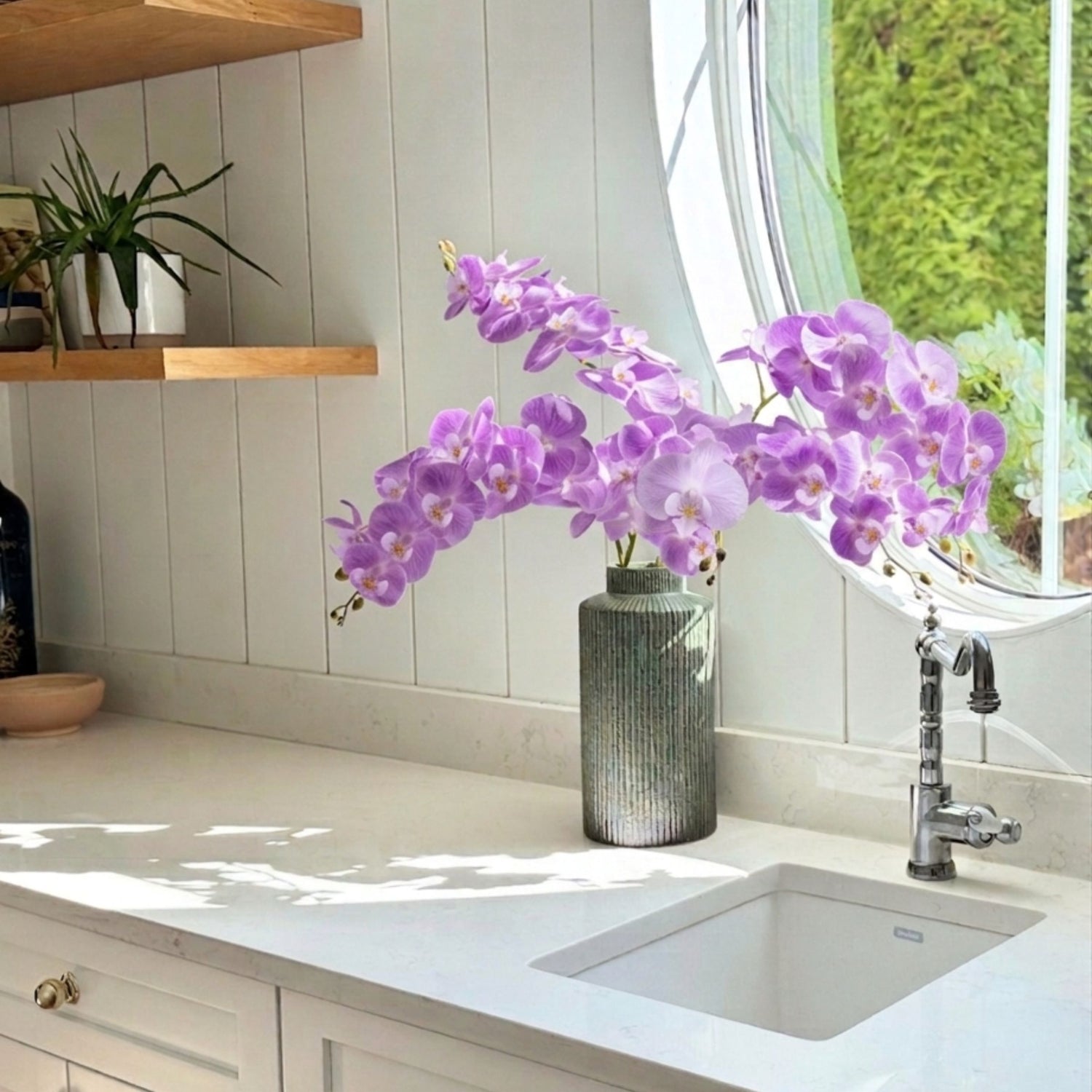 Purple artificial orchids in a vase on a kitchen counter with a window in the background - for My Faux Florist Canada.