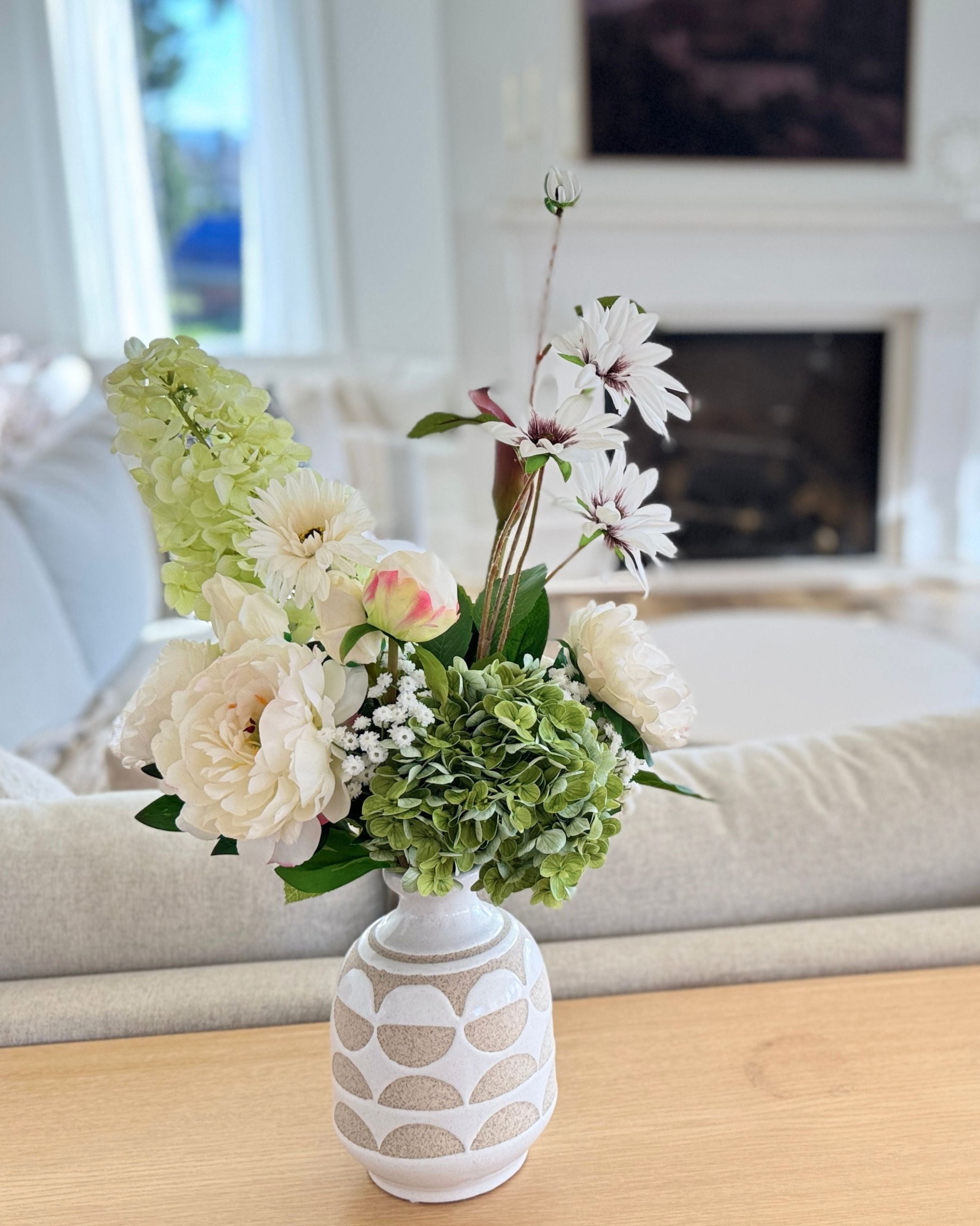Floral arrangement of realistic artificial flowers in a patterned vase on a table with a blurred indoor background. Faux peonies, faux roses, faux hydrangea, in an artificial flower bouquet for My Faux Florist Canada.