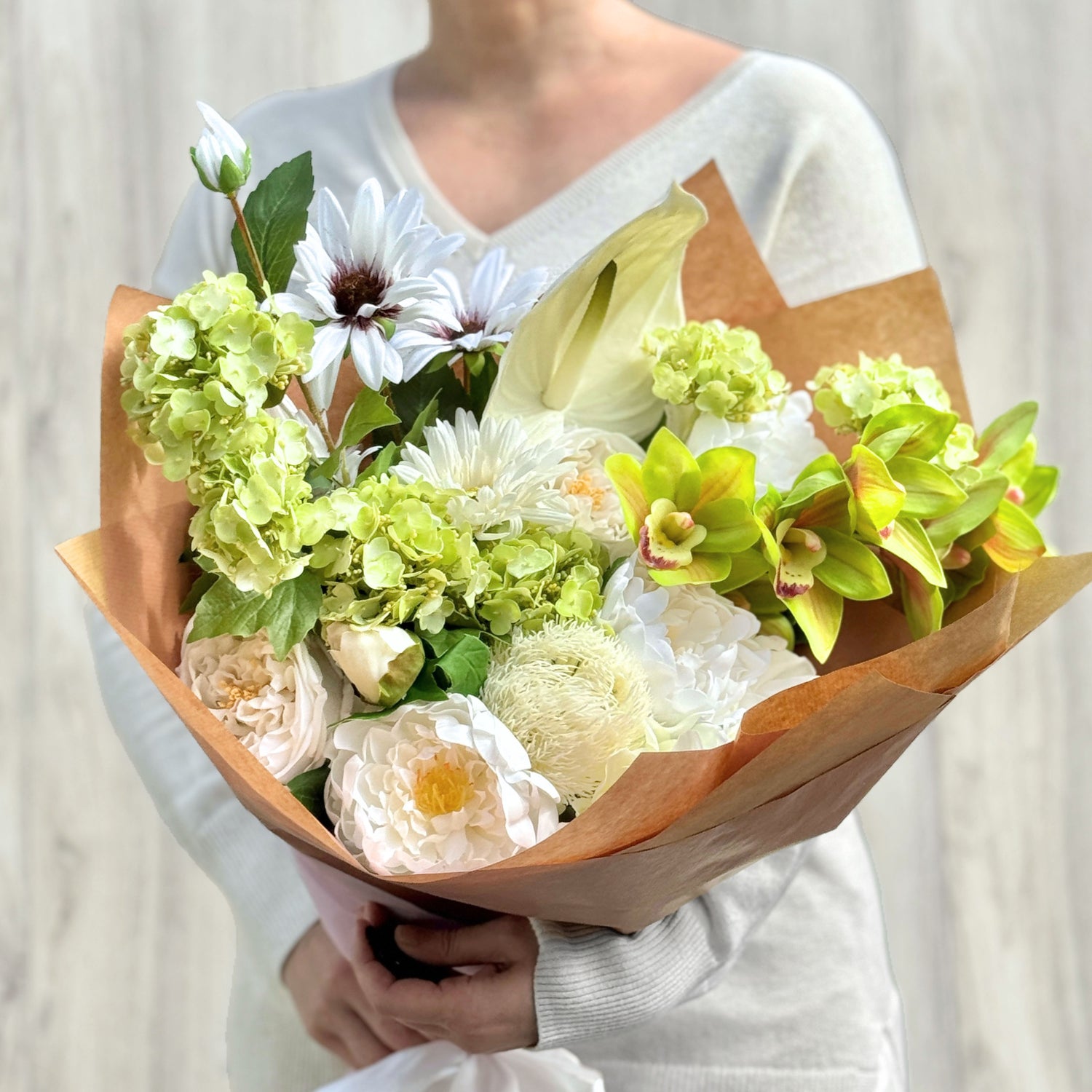 Bouquet of realistic artificial flowers wrapped in brown paper held by a person wearing a white sweater. Faux peonies, faux roses, faux hydrangea, and faux orchids in an artificial flower bouquet for My Faux Florist Canada.