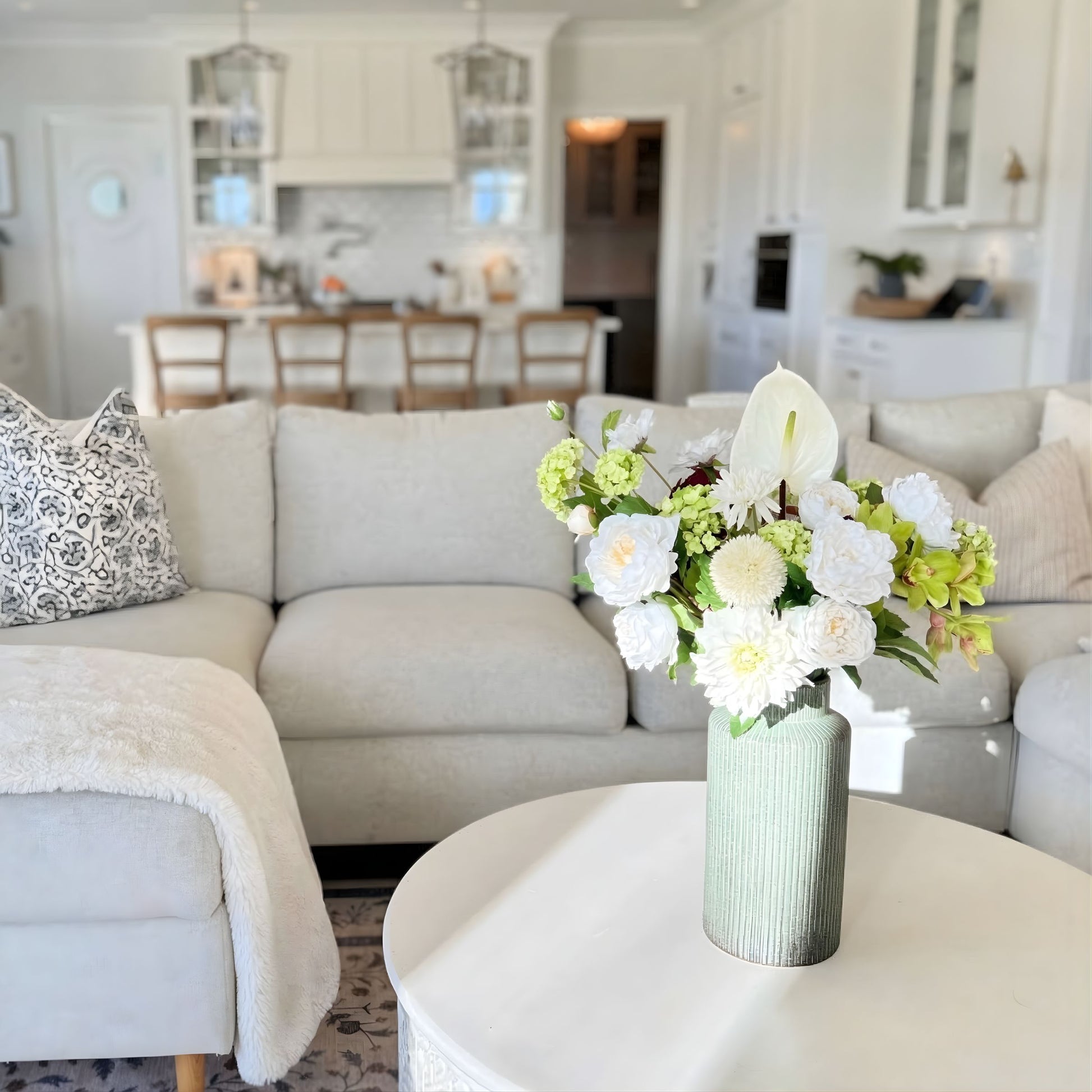 Floral arrangement of realistic artificial flowers in a living room with a couch and coffee table. Faux peonies, faux roses, faux hydrangea, and faux orchids in an artificial flower bouquet for My Faux Florist Canada.