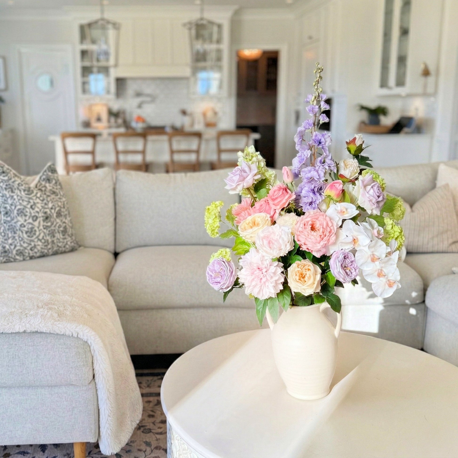 Floral arrangement  of realistic artificial flowers in a vase on a coffee table in a living room. Faux peonies, faux roses, faux hydrangea, and faux orchids in an artificial flower bouquet for My Faux Florist Canada.