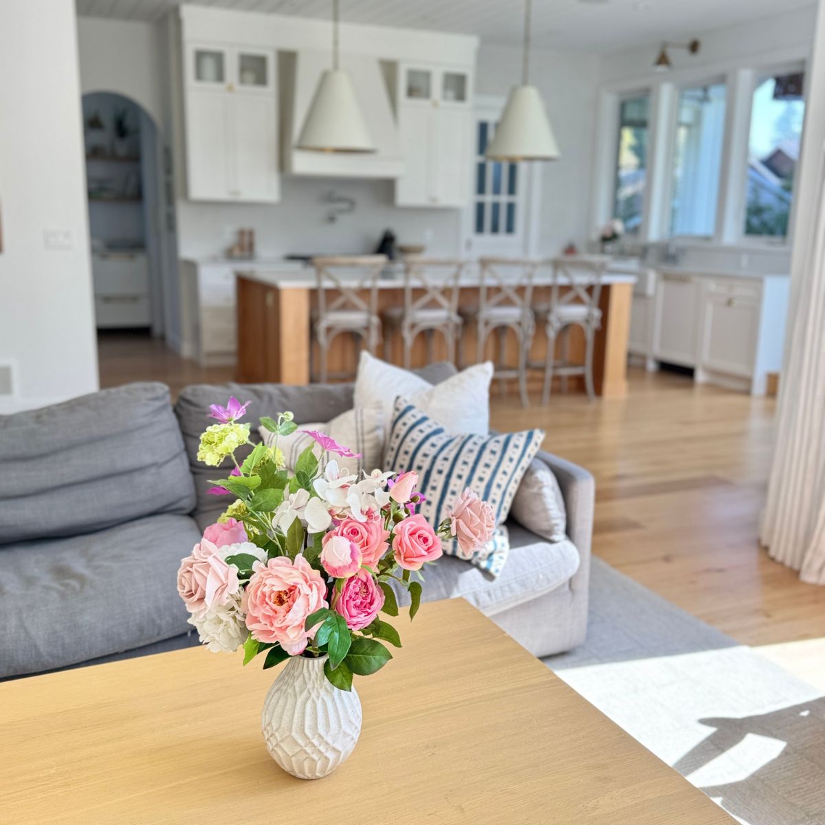 Floral arrangement of realistic artificial flowers in a vase on a coffee table in a living room. Faux peonies, faux roses, faux hydrangea, in an artificial flower bouquet for My Faux Florist Canada.