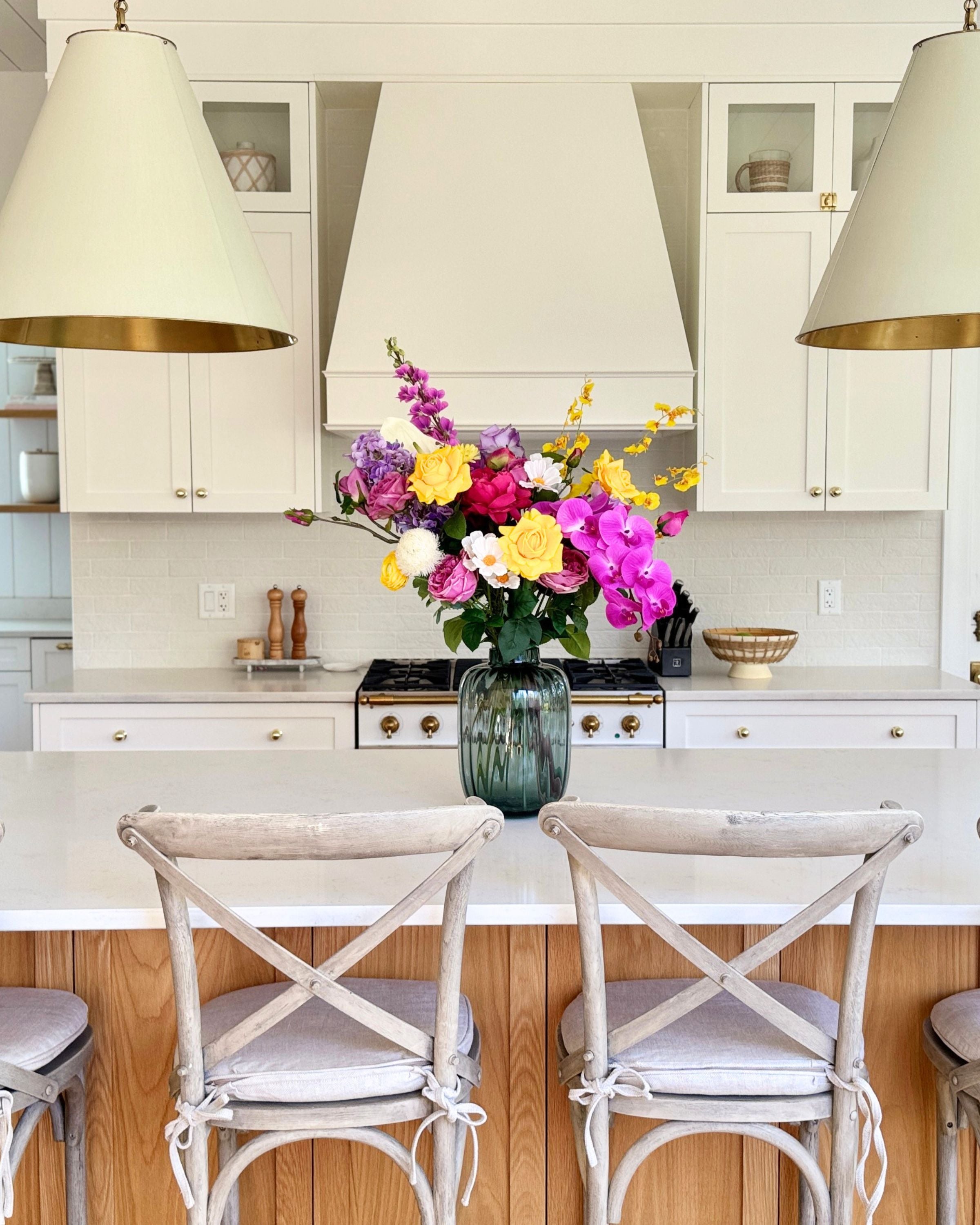 Kitchen with white cabinets, a stove, and a vase of colorful realistic artificial flowers on the counter. Faux peonies, faux roses, faux hydrangea, and faux orchids in an artificial flower bouquet for My Faux Florist Canada.