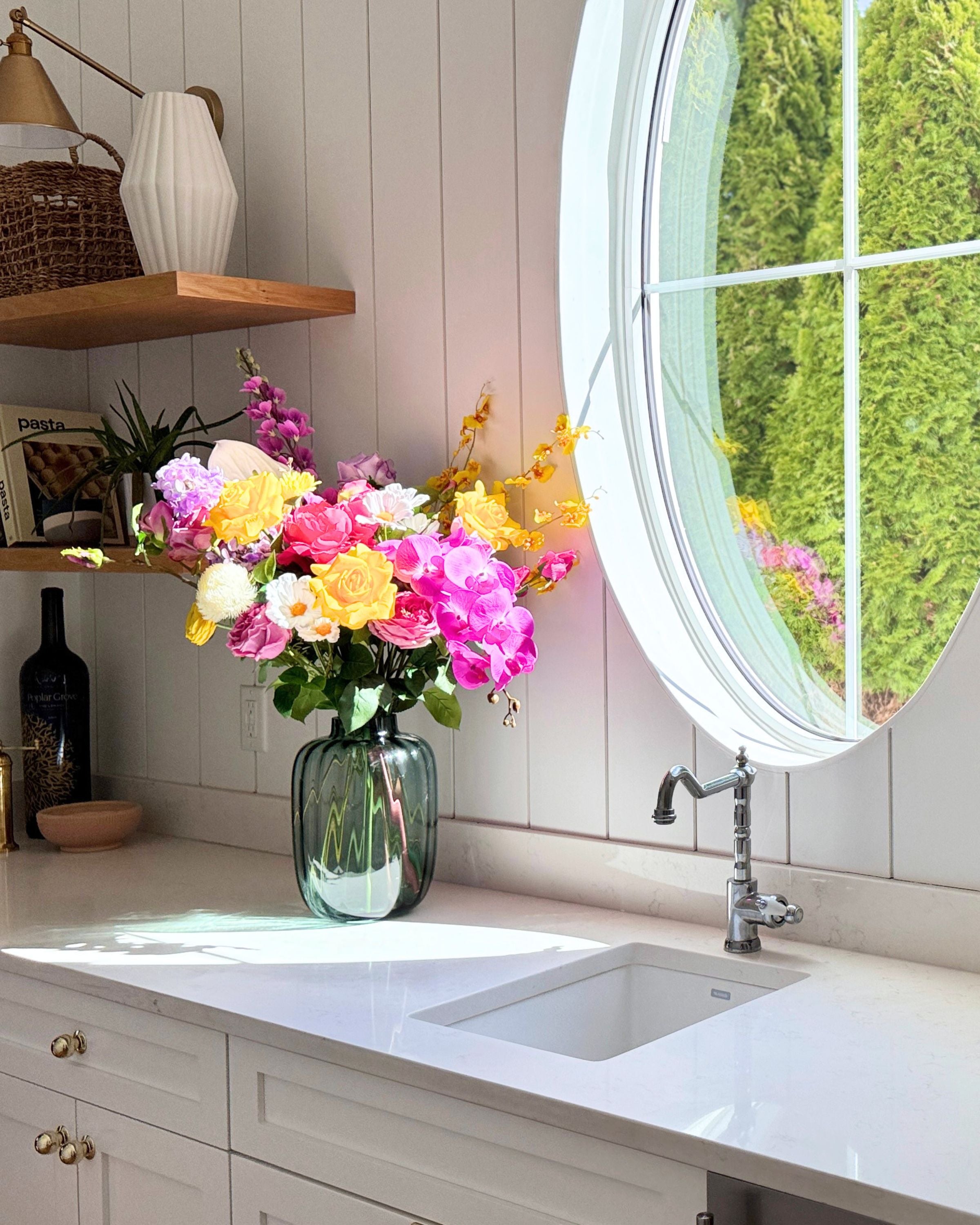 Kitchen with a sink, colorful and realistic artificial flowers in a vase, and a round window. Faux peonies, faux roses, faux hydrangea, and faux orchids in an artificial flower bouquet for My Faux Florist Canada.