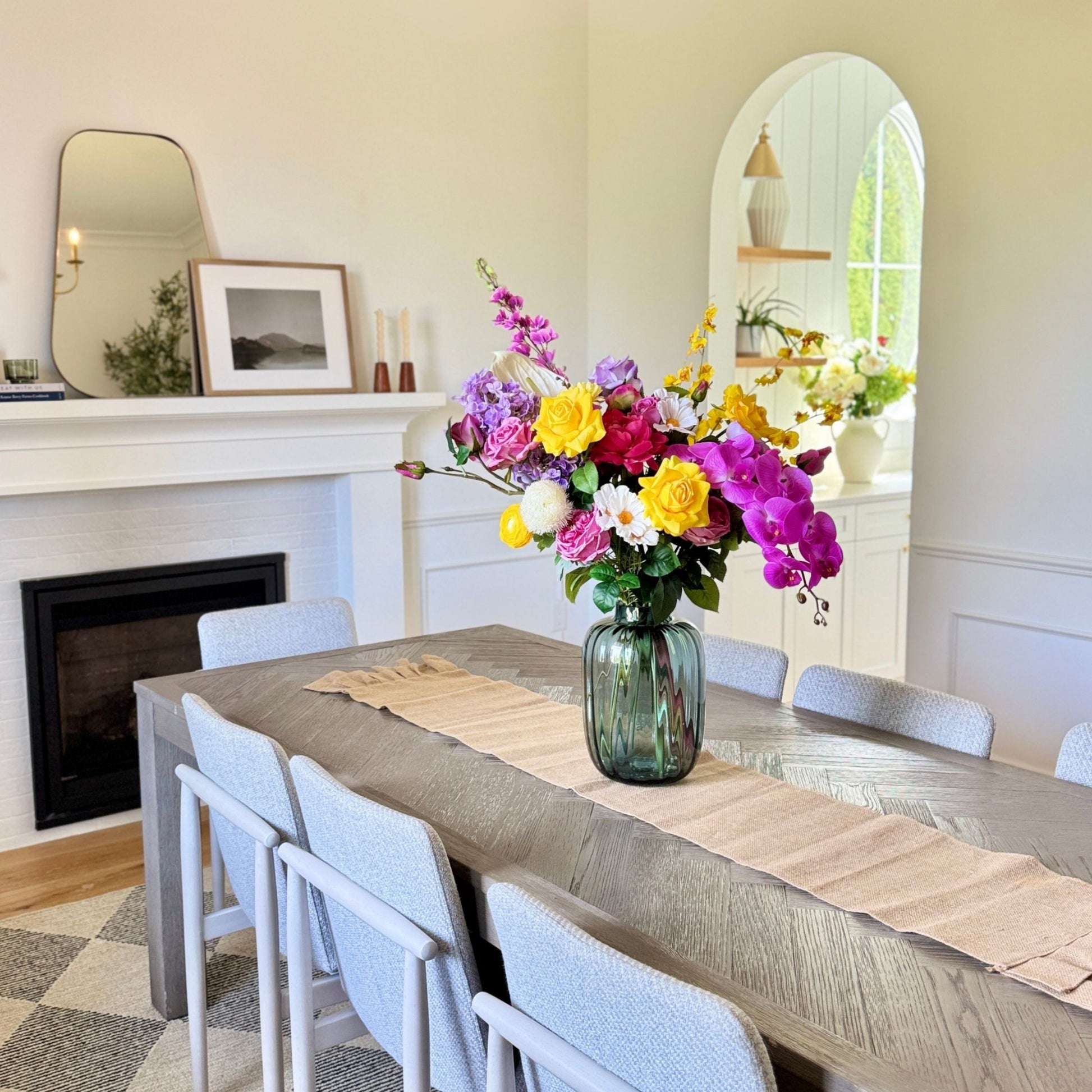 Dining room with a table set for a meal, realistic artificial flowers in a vase, and a fireplace. Faux peonies, faux roses, faux hydrangea, and faux orchids in an artificial flower bouquet for My Faux Florist Canada.
