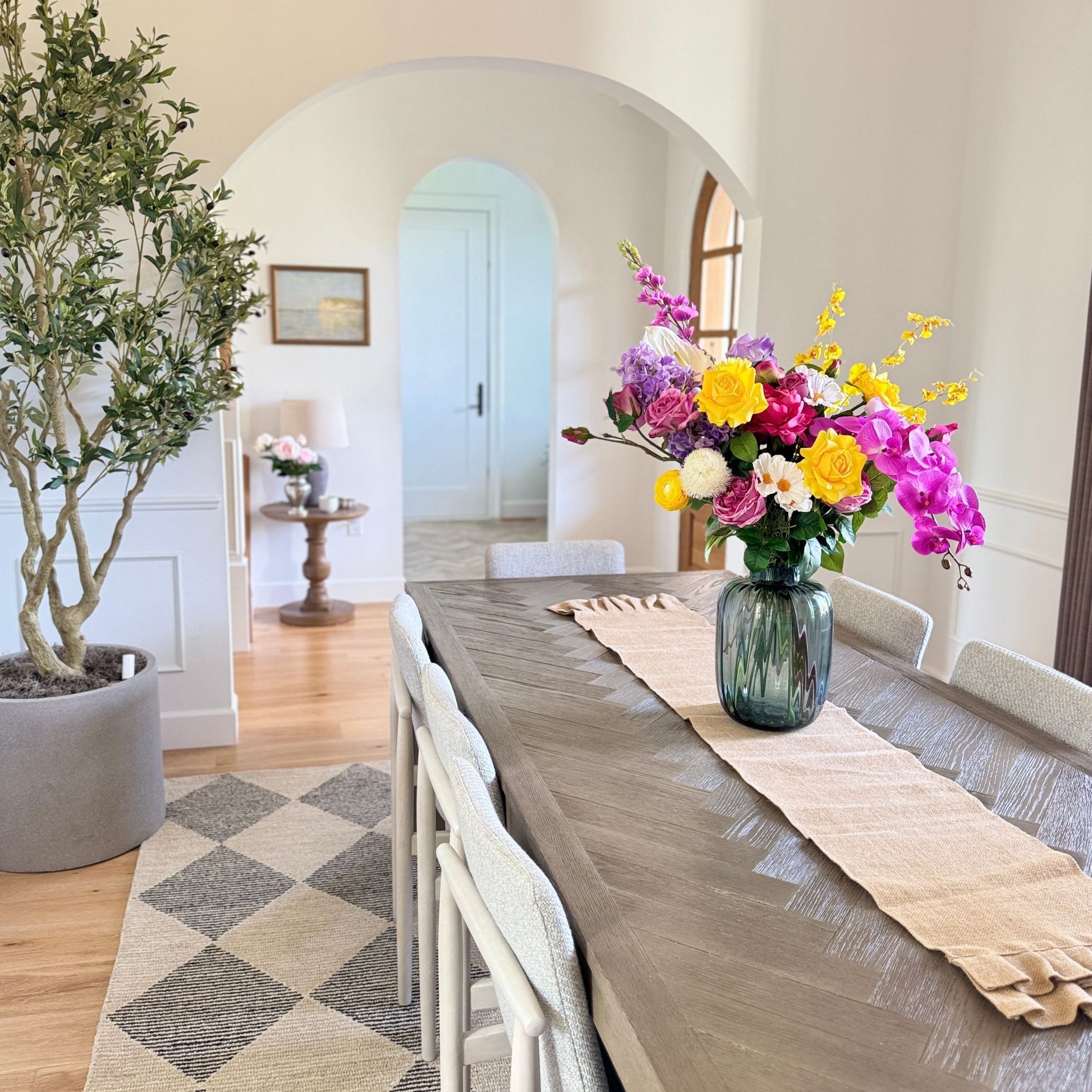 Dining room with a long table set for a meal, featuring a vase of colorful and realistic artificial flowers. Faux peonies, faux roses, faux hydrangea, and faux orchids in an artificial flower bouquet for My Faux Florist Canada.