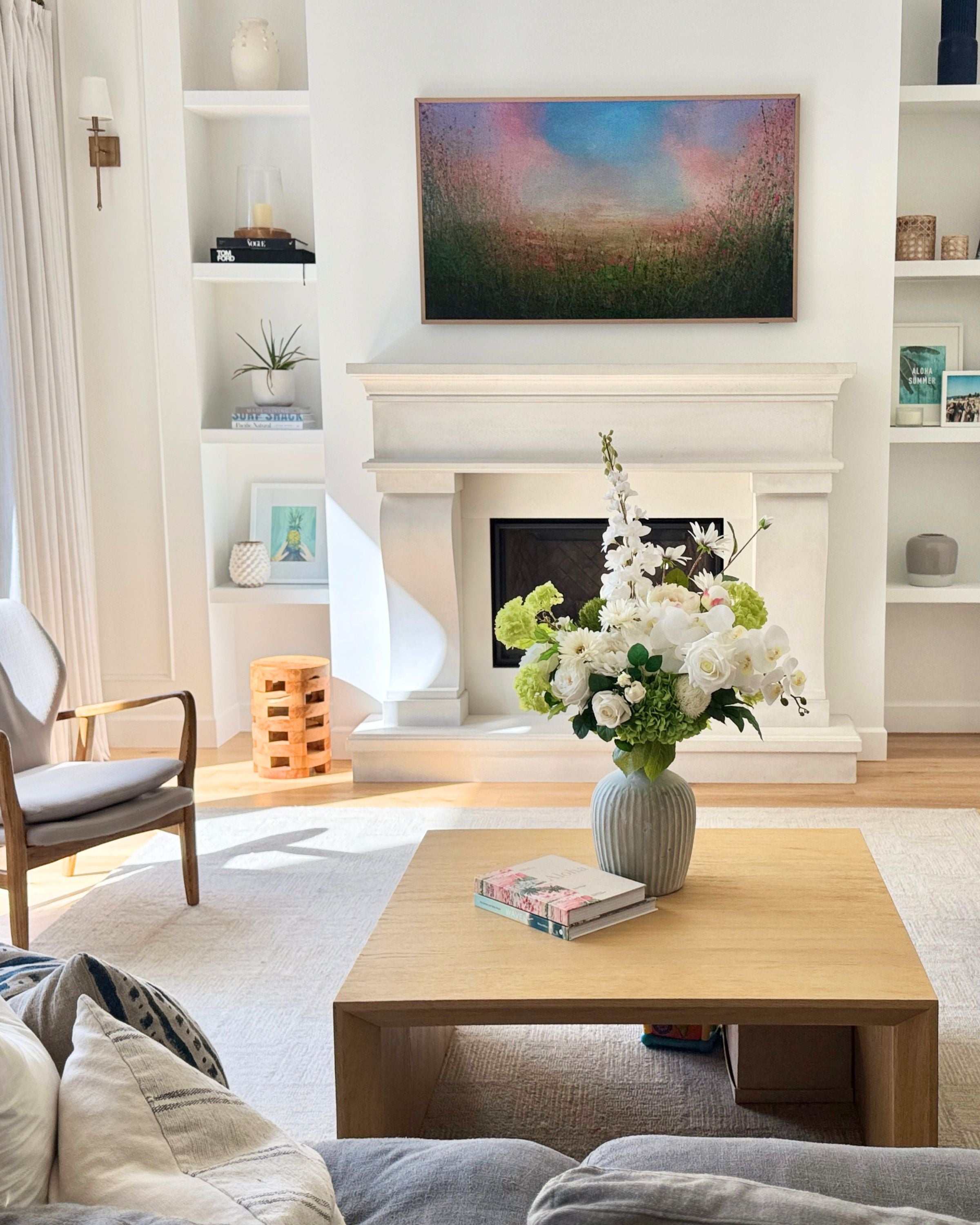 Living room with a fireplace, coffee table, and decorative elements including a large vase of realistic artificial flowers in white and green on the table. Faux peonies, faux roses, faux hydrangea, and faux orchids in an artificial flower bouquet for My Faux Florist Canada.