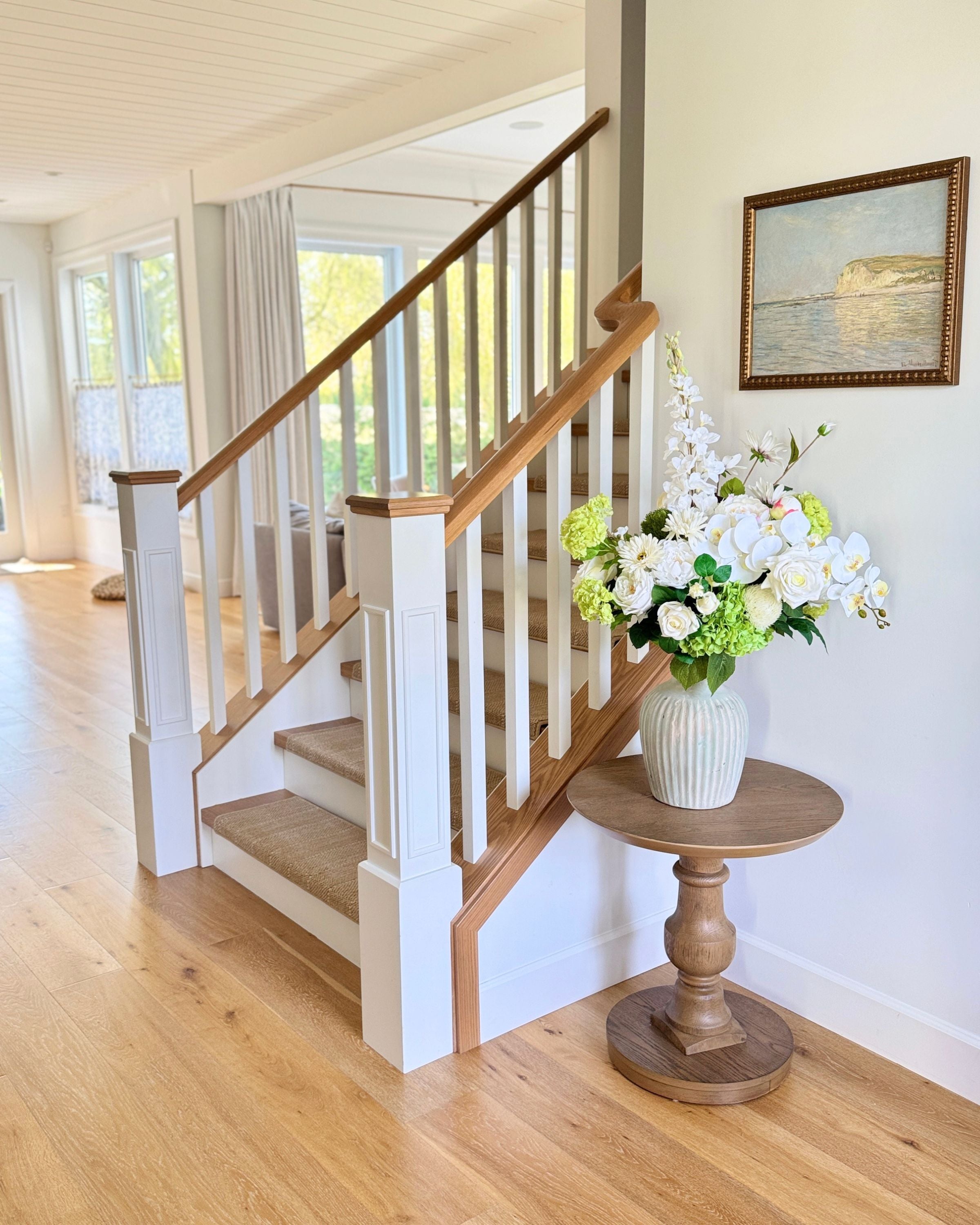 Staircase with wooden handrail and white balusters, featuring a vase of realistic artificial flowers on a small table. Faux peonies, faux roses, faux hydrangea, and faux orchids in an artificial flower bouquet for My Faux Florist Canada.