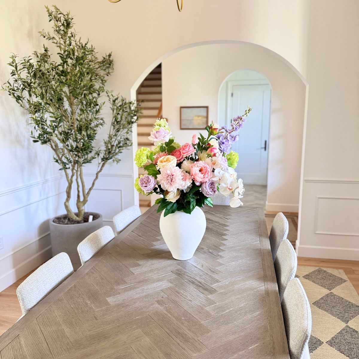 Dining room with a long wooden table, white chairs, and a vase of realistic artificial flowers. Faux peonies, faux roses, faux hydrangea, and faux orchids in an artificial flower bouquet for My Faux Florist Canada.