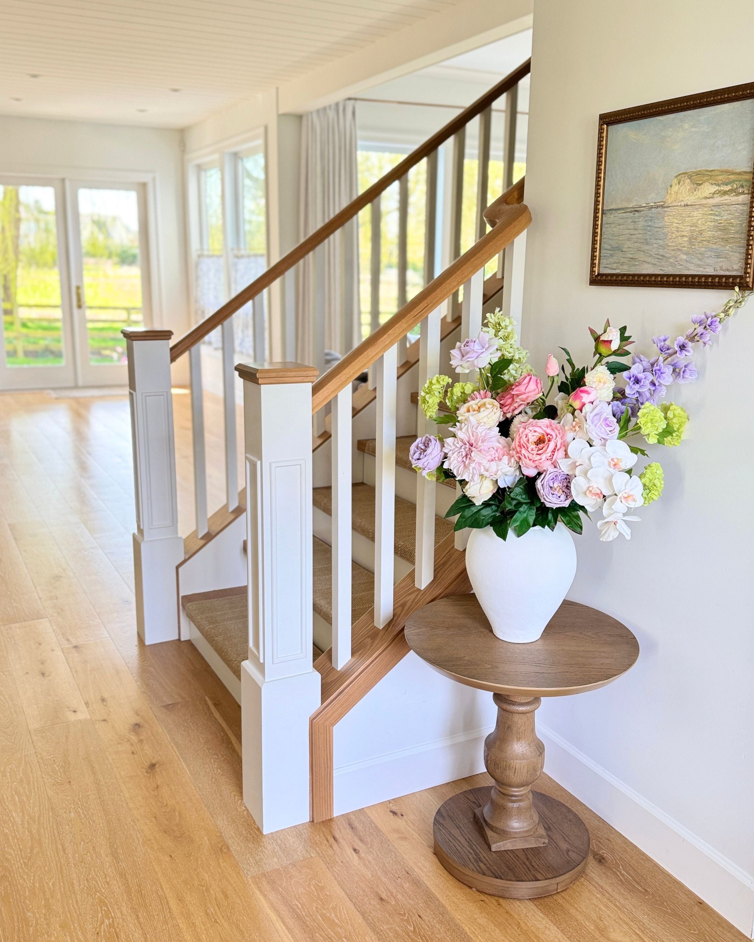 Staircase with a vase of realistic artificial flowers on a wooden table in a bright room. Faux peonies, faux roses, faux hydrangea, and faux orchids in an artificial flower bouquet for My Faux Florist Canada.