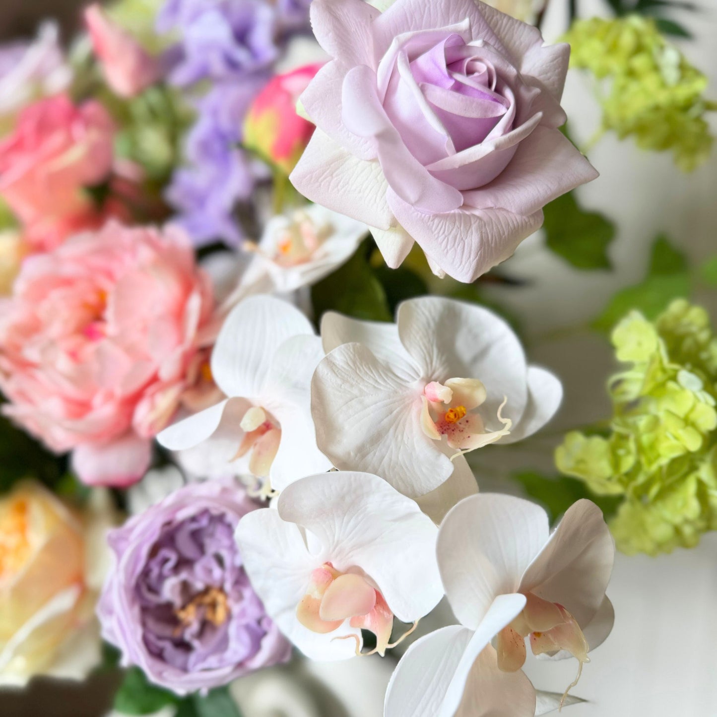 Bouquet of flowers including roses and orchids with a blurred background. Realistic artificial flowers. Faux peonies, faux roses, faux hydrangea, and faux orchids in an artificial flower bouquet for My Faux Florist Canada.