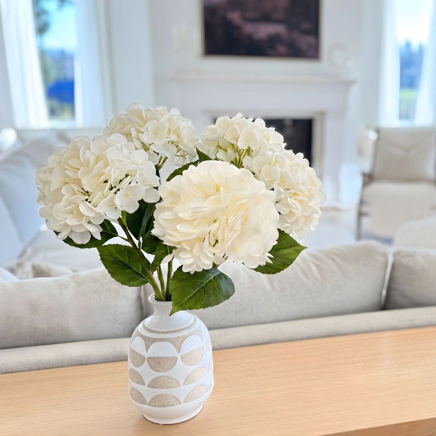 White realistic artificial hydrangeas in a patterned vase on a wooden table in a living room- for My Faux Florist Canada.