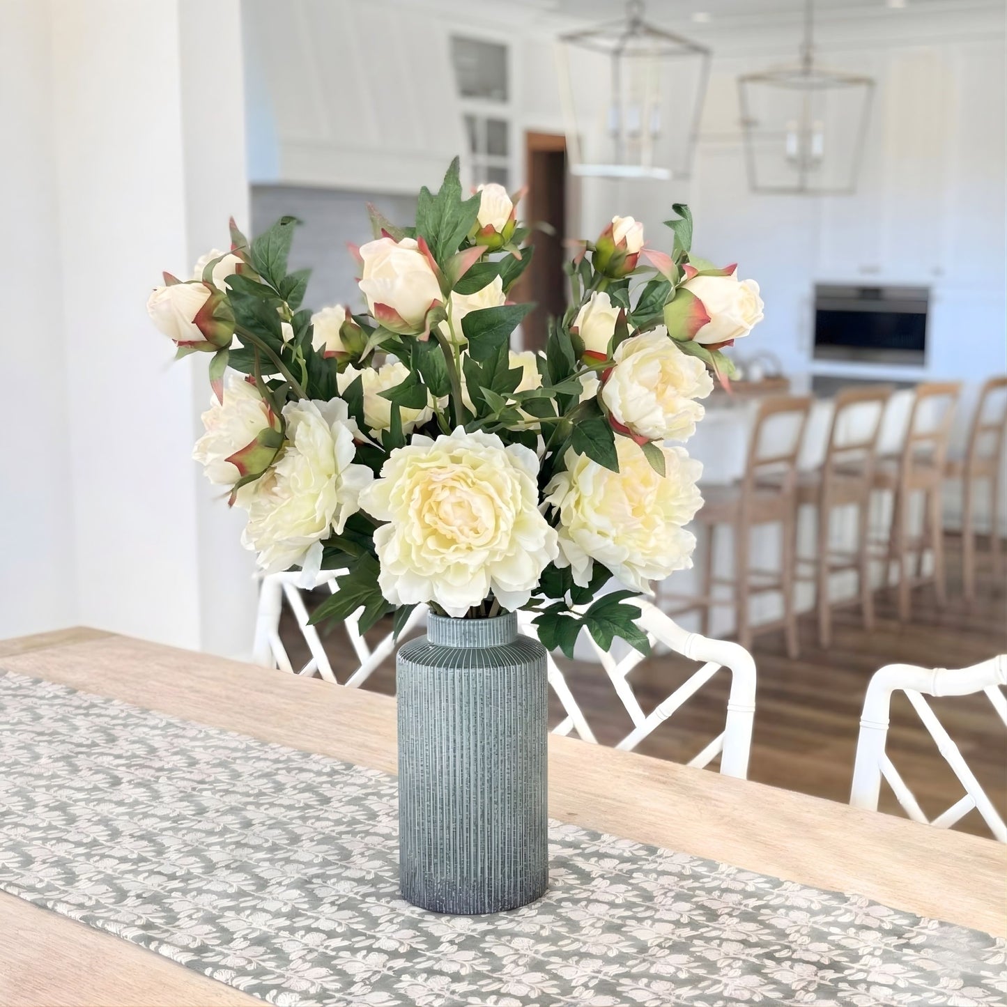 Bouquet of white and green realistic artificial peonies in a gray vase on a dining table with a kitchen in the background. For My Faux Florist Canada