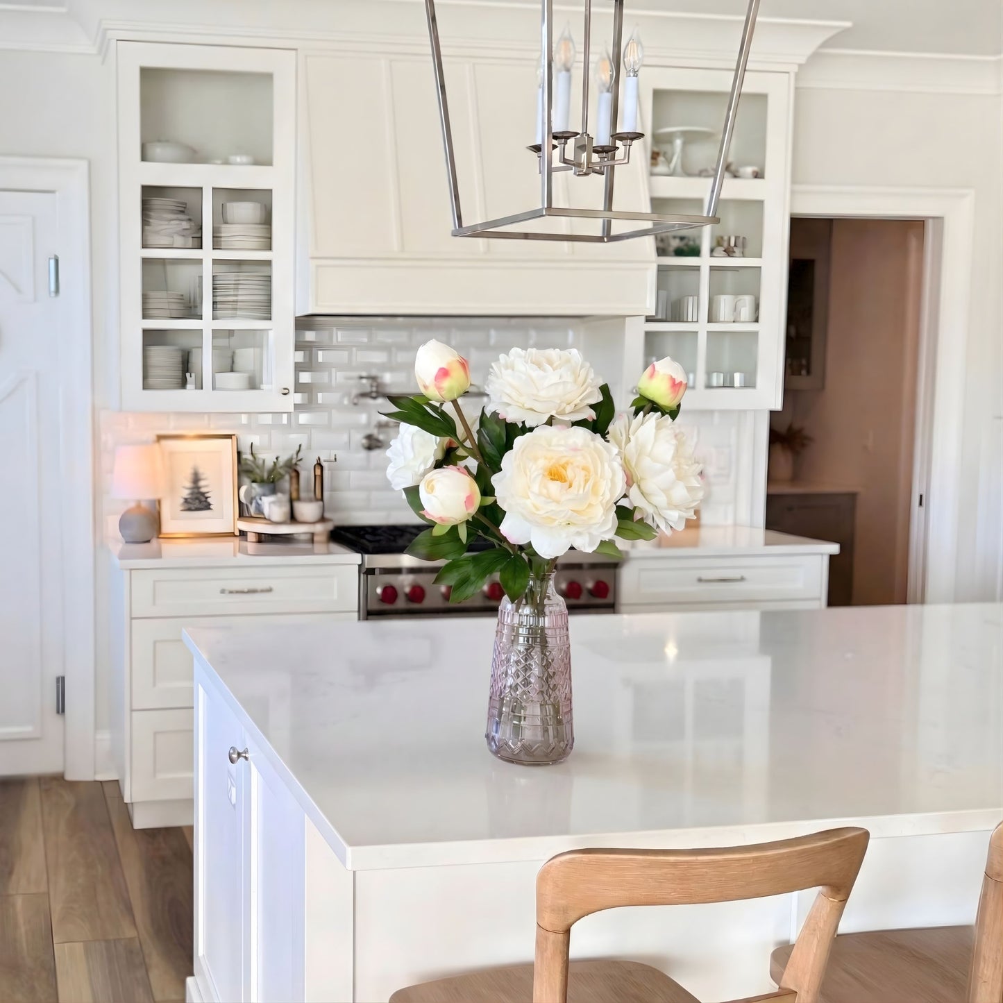 Modern kitchen with white cabinets, a vase of realistic artificial peonies on the counter, and a chandelier. For My Faux Florist Canada.