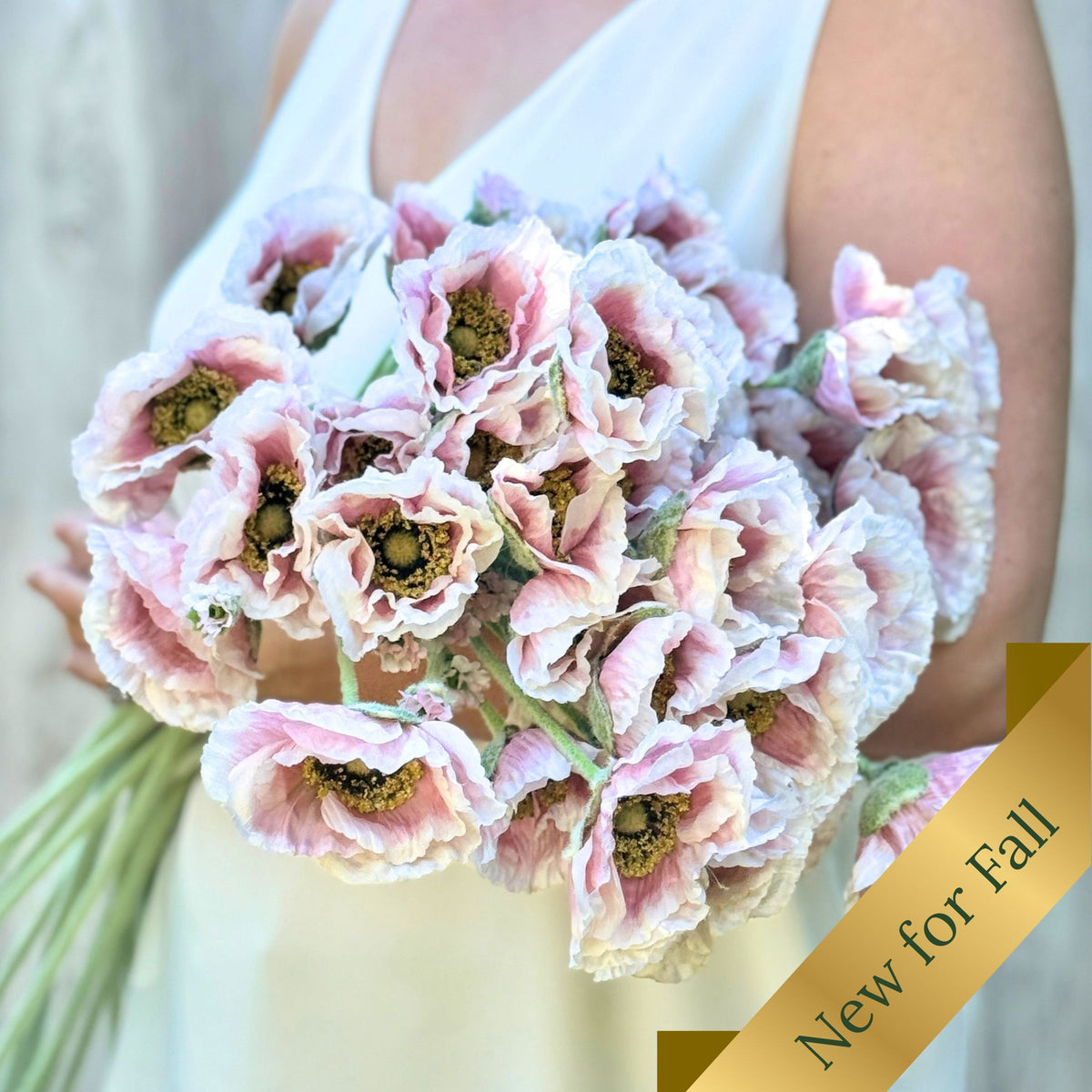 A close-up of a person holding a bouquet of pale pink and white realistic silk poppies with dark centers, wearing a white sleeveless top. A gold diagonal banner in the lower right reads 'New for Fall'. For My Faux Florist Canada.