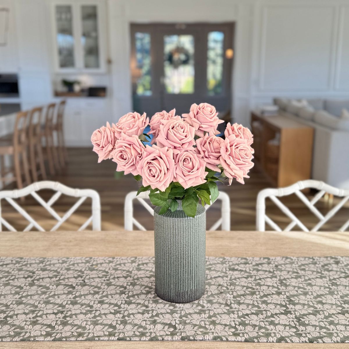 Pink artificial roses in a vase on a table in a room with chairs and a door - for My Faux Florist Canada.