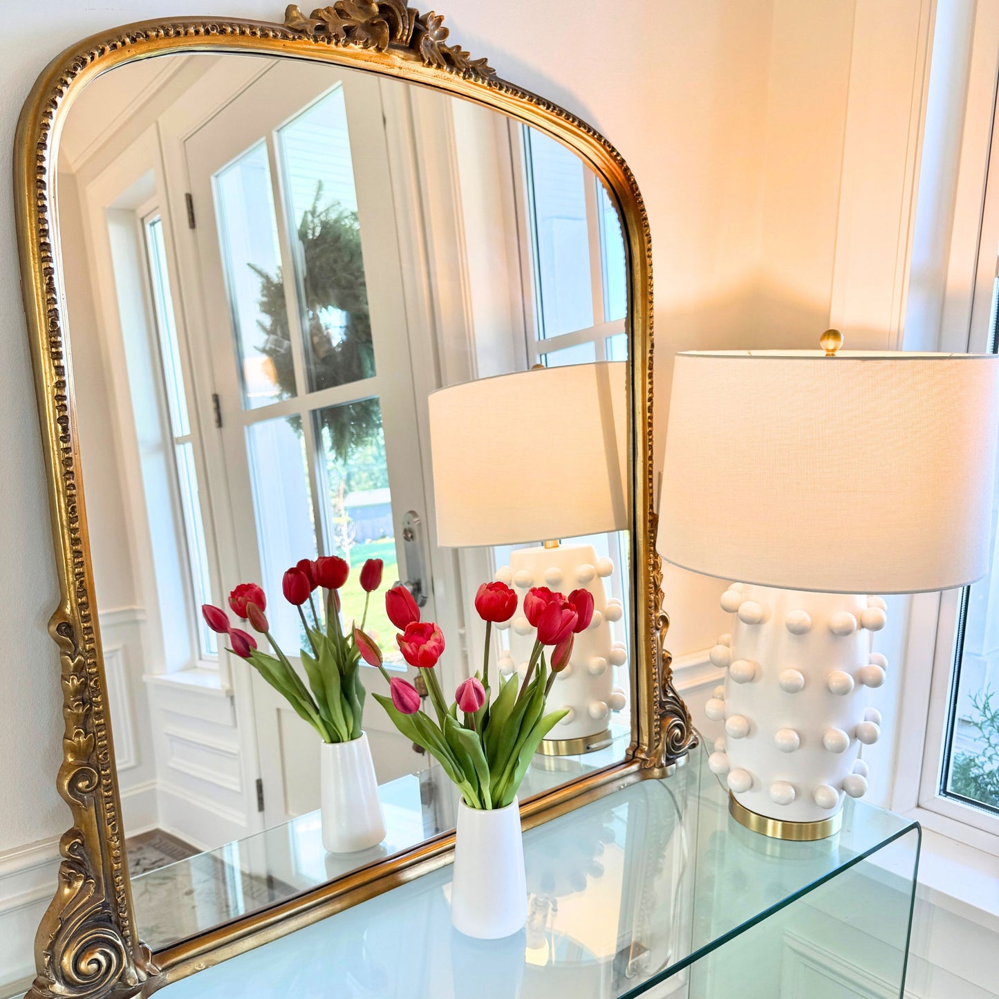 Decorative mirror with gold frame on a glass table with pink artificial tulips and lamps,  for My Faux Florist Canada.