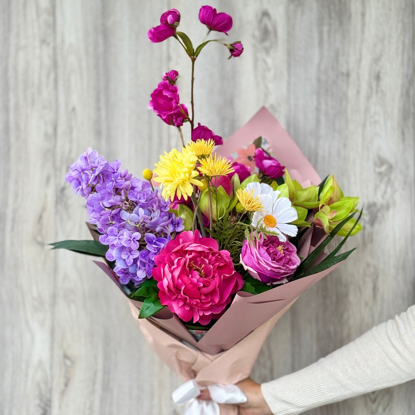Bouquet of colorful artificial flowers held by a person against a neutral background - bouquets includes artificial orchids artificial roses, artificial peonies, real touch flowers from my faux florist canada.