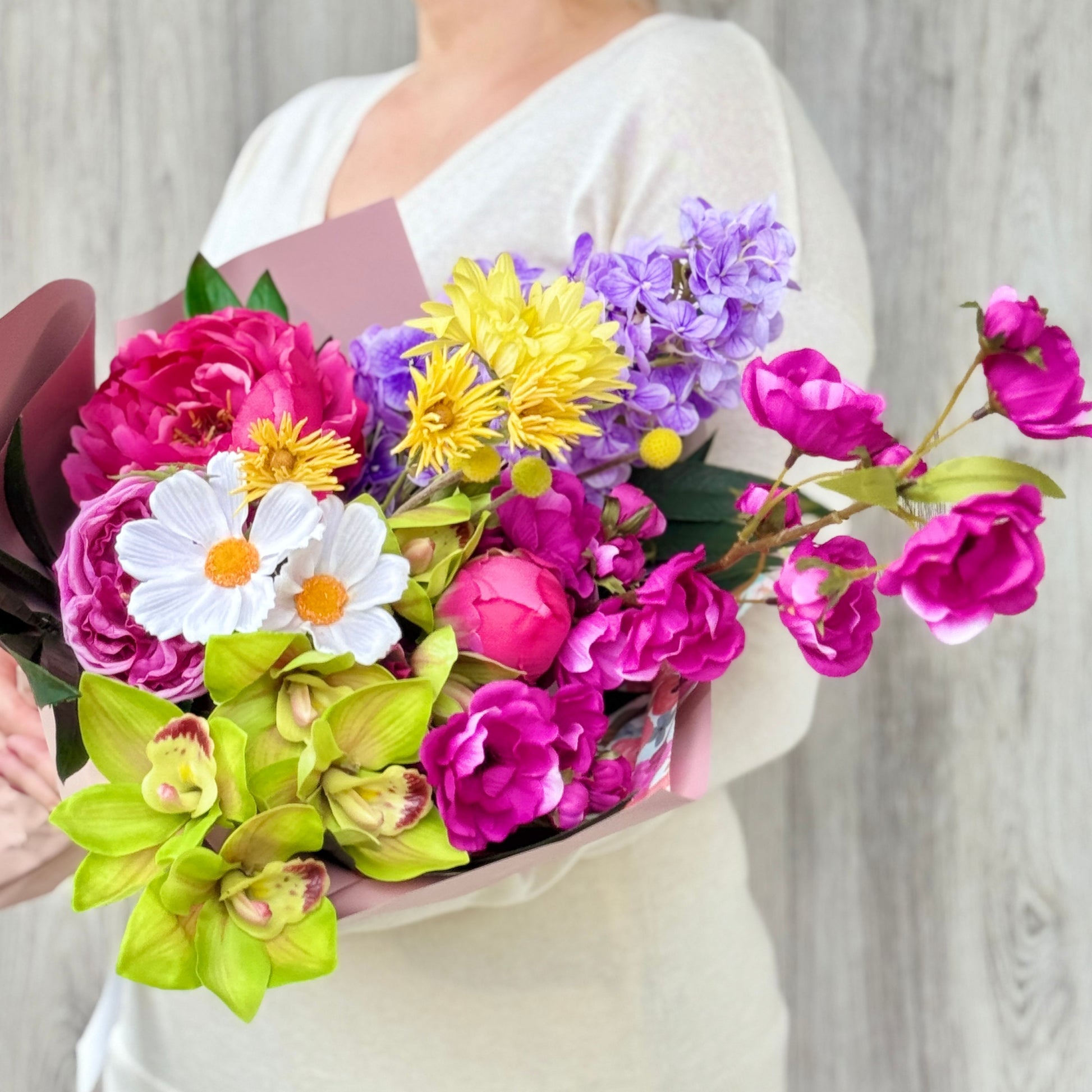 Bouquet of colorful artificial flowers held by a person against a neutral background - bouquets includes artificial orchids artificial roses, artificial peonies, real touch flowers from my faux florist canada.