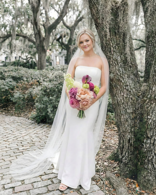 Bride standing outdoors holding an artificial wedding bouquet of realistic artificial flowers in peaches, whites and pinks from My Faux Florist Canada.